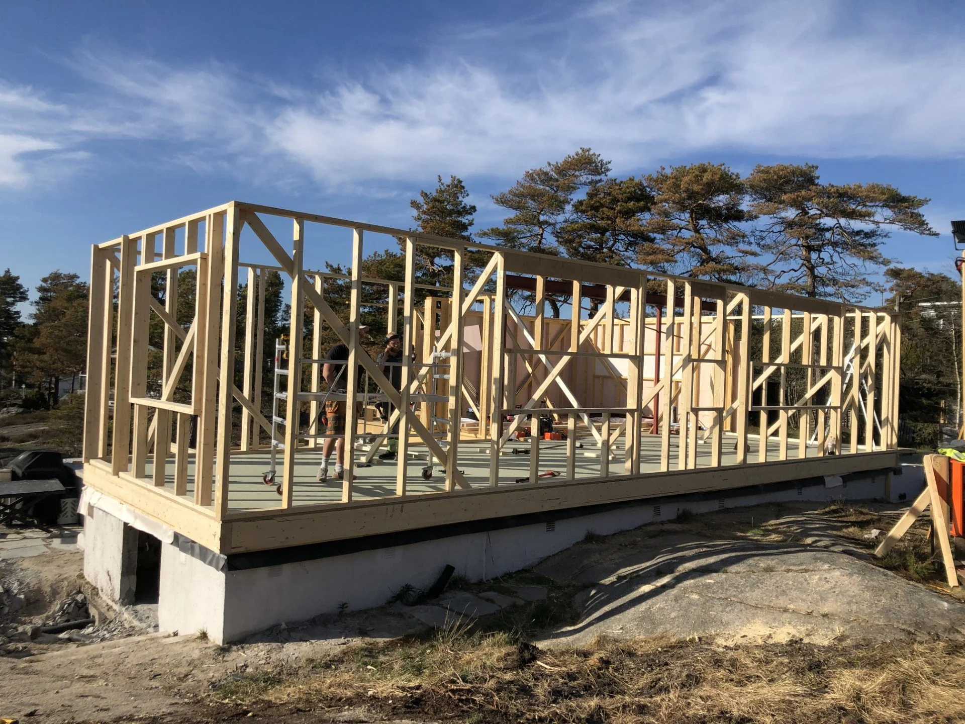 Rammeverk av tre som bygges på en betongplate ute i naturen med trær i bakgrunnen.