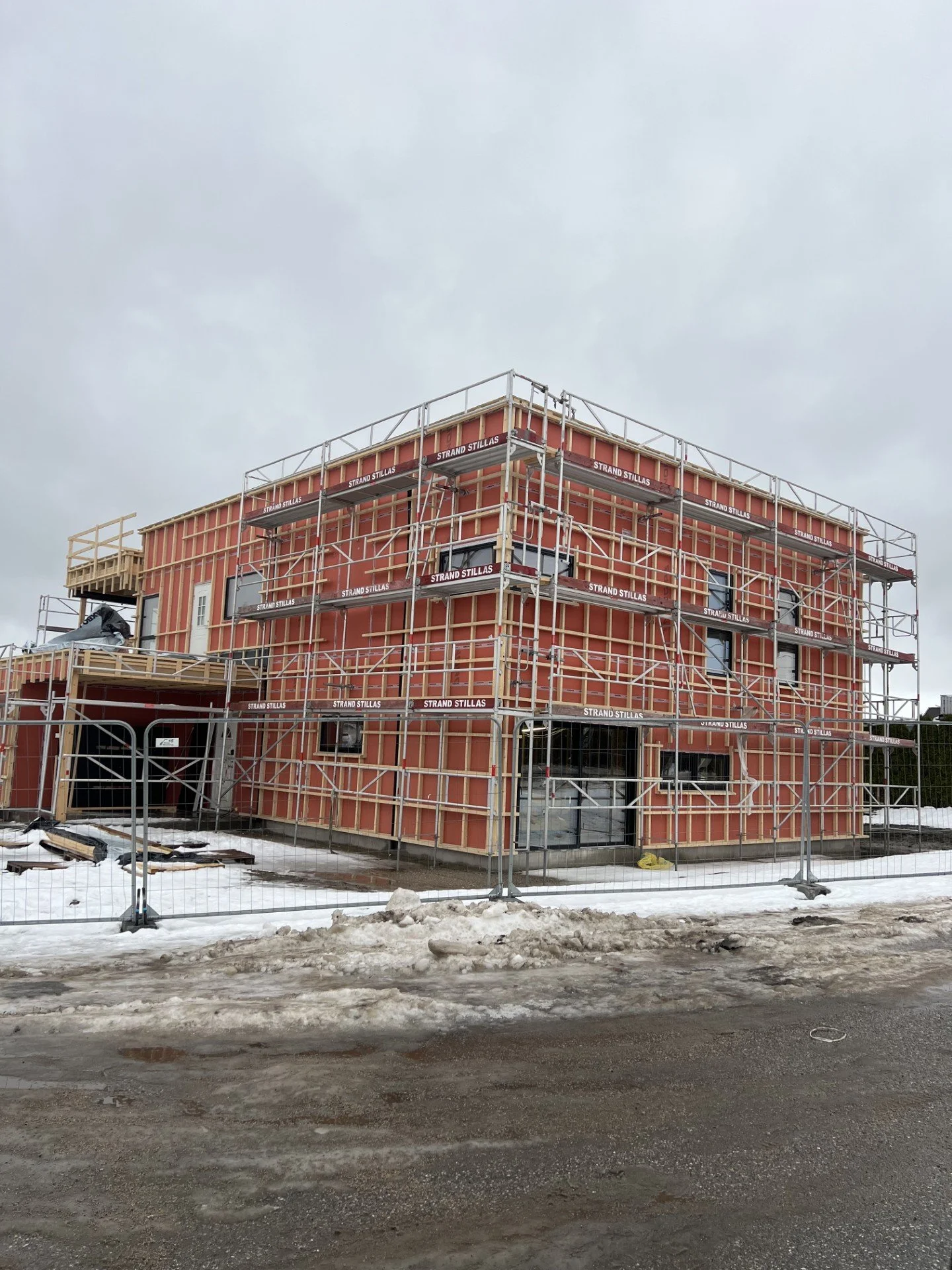 Nybygget hus under konstruksjon med scaffolding rundt, snø og skitten vei foran.
