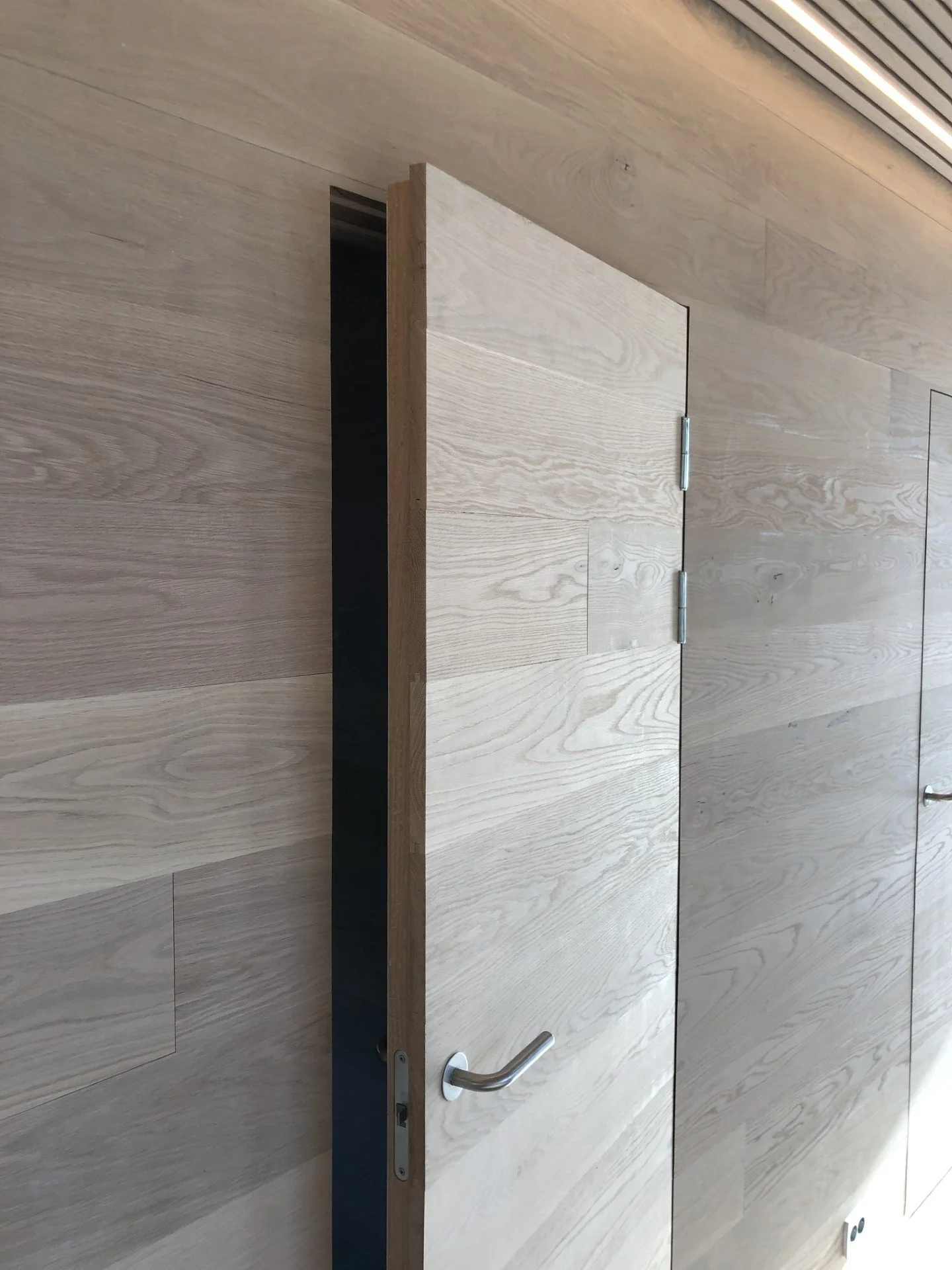 Lukket dør i tre med stållås og håndtak, plassert på en vegg av trepanel.