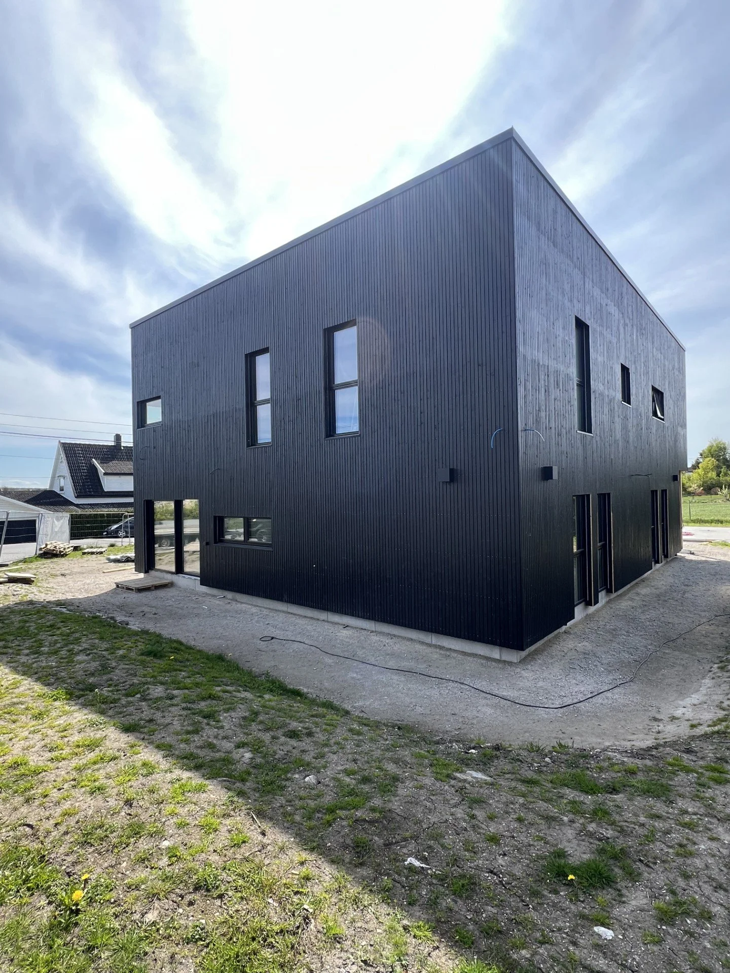 En moderne, svart bygning med flere vinduer under en blå himmel med noen skyer.