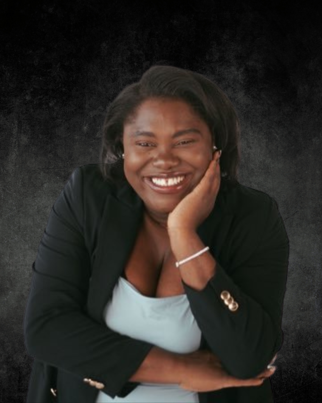 A person laughing with her hand on her face, wearing a black blazer over a light-colored top, against a dark textured background.