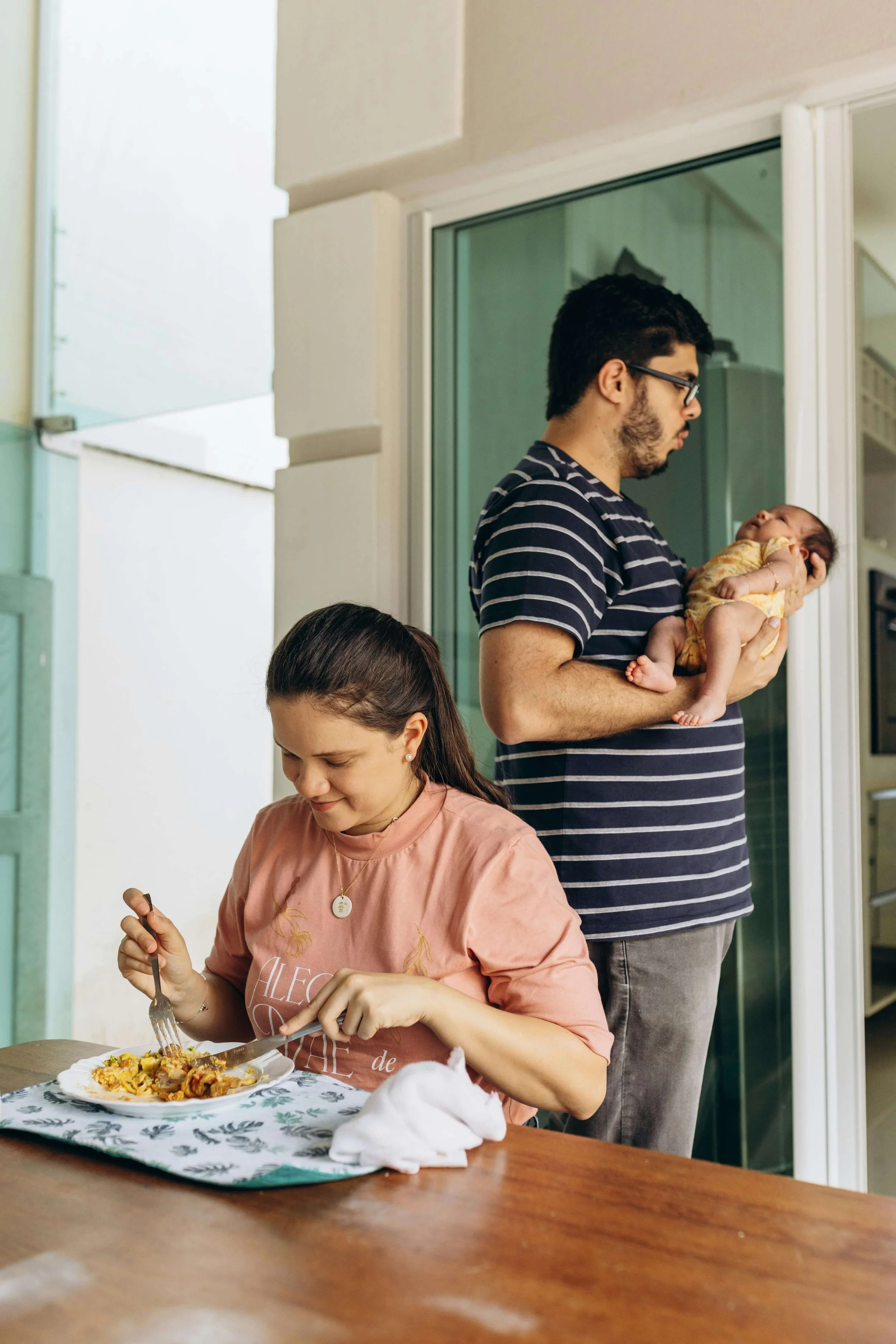 New mom eats a meal while dad holds their infant baby.