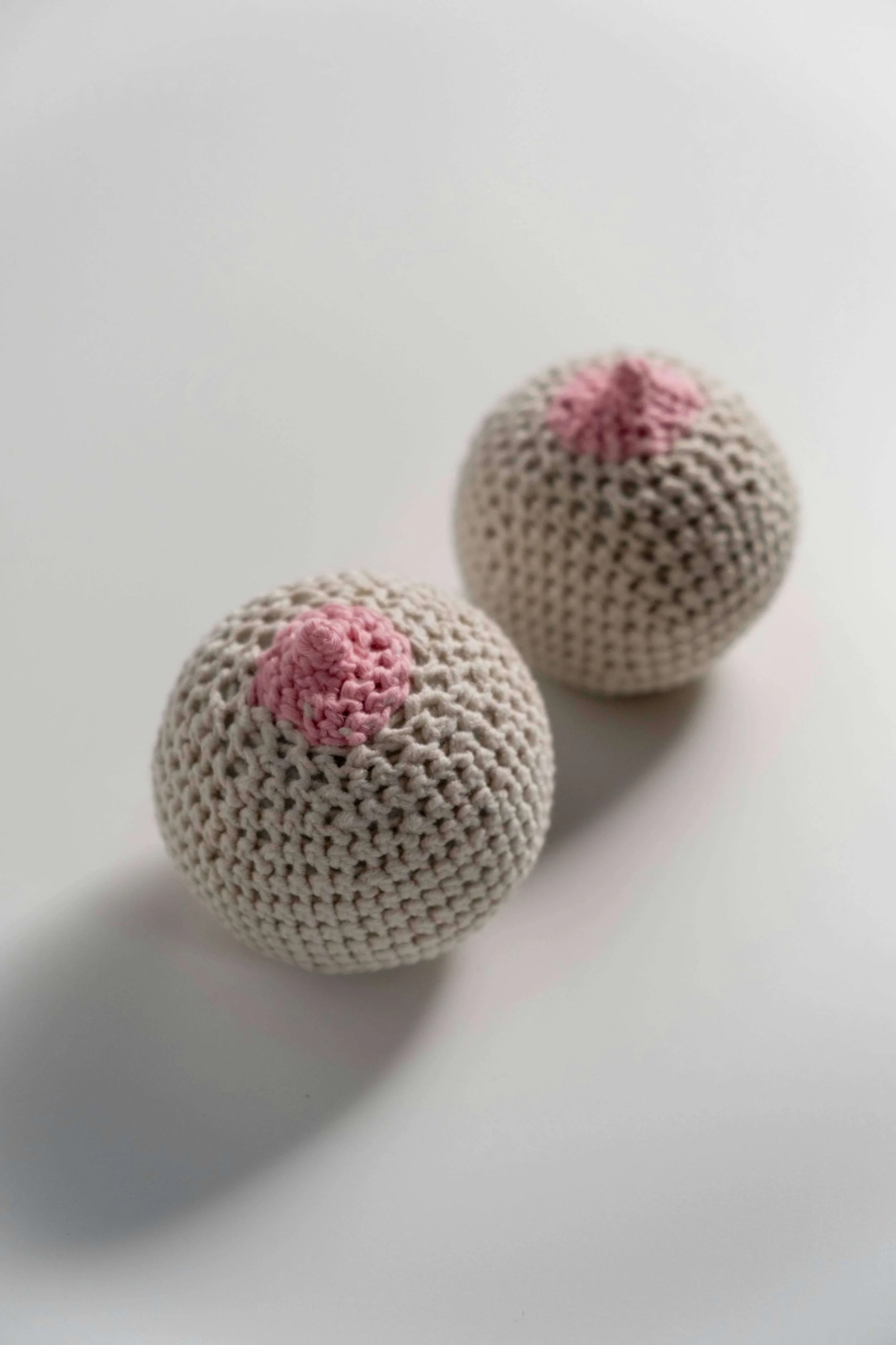 Two crocheted tan spheres with pink areas to look nipples are breast models used in lactation classes.