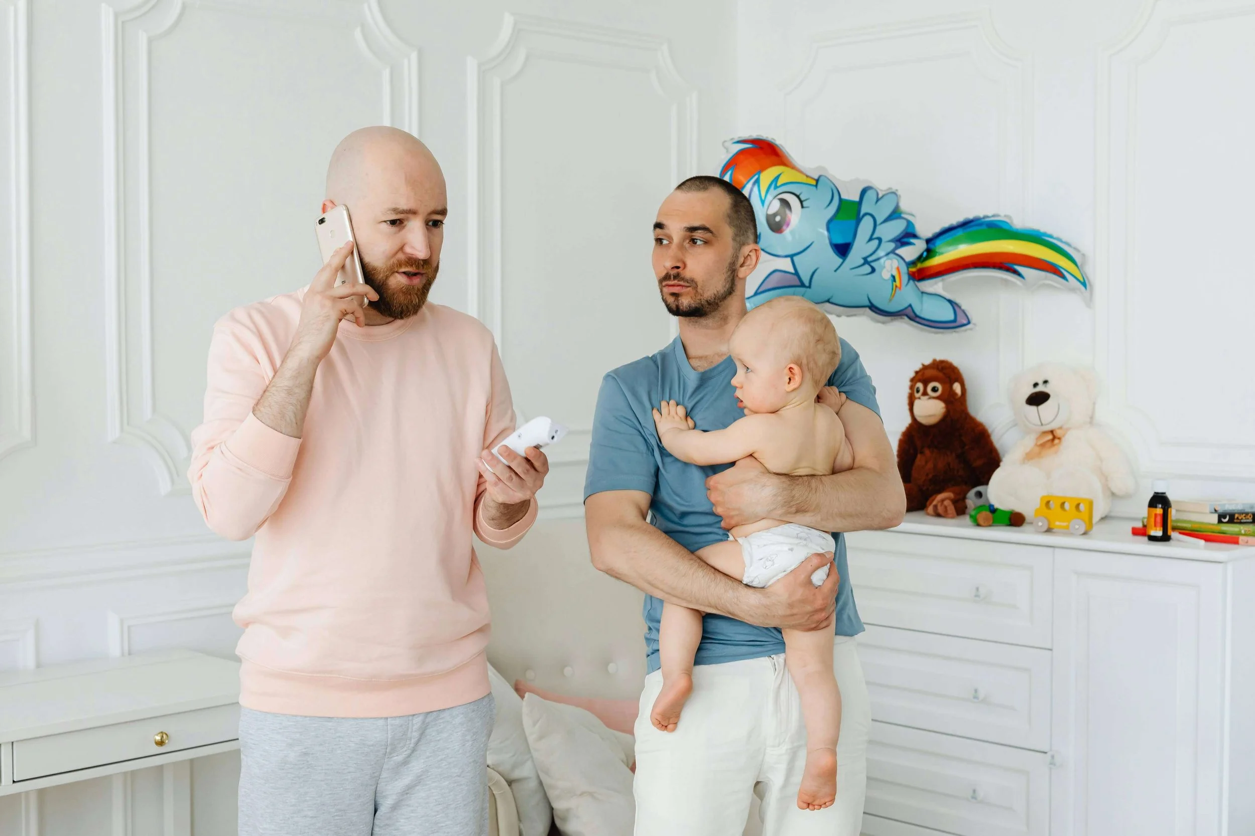 Dad on cell phone while partner holds their new baby in the nursery.