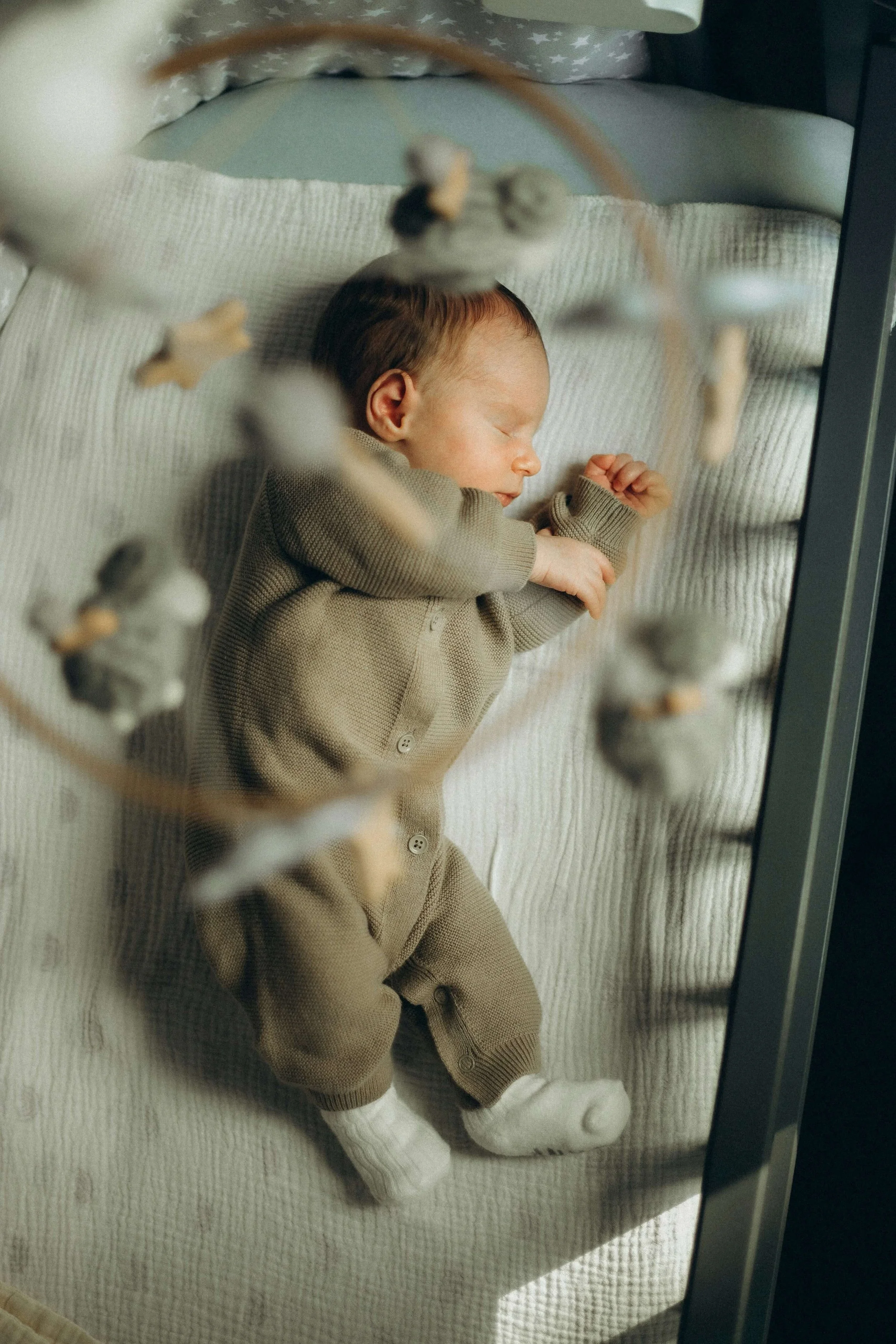 An infant sleeps peacefully in their crib with a mobile hanging above them.
