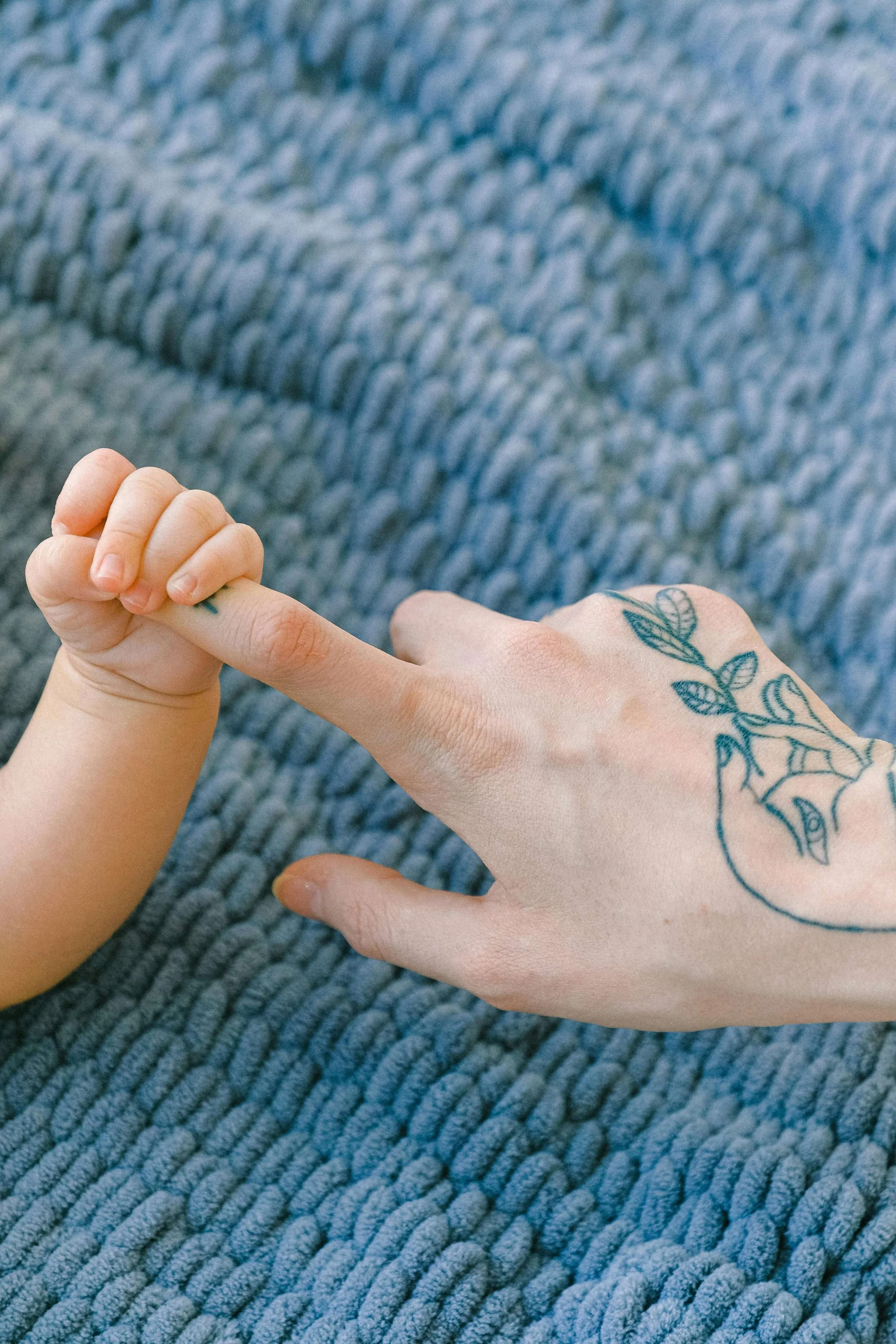 Infant holds moms hand in front of blue blanket.