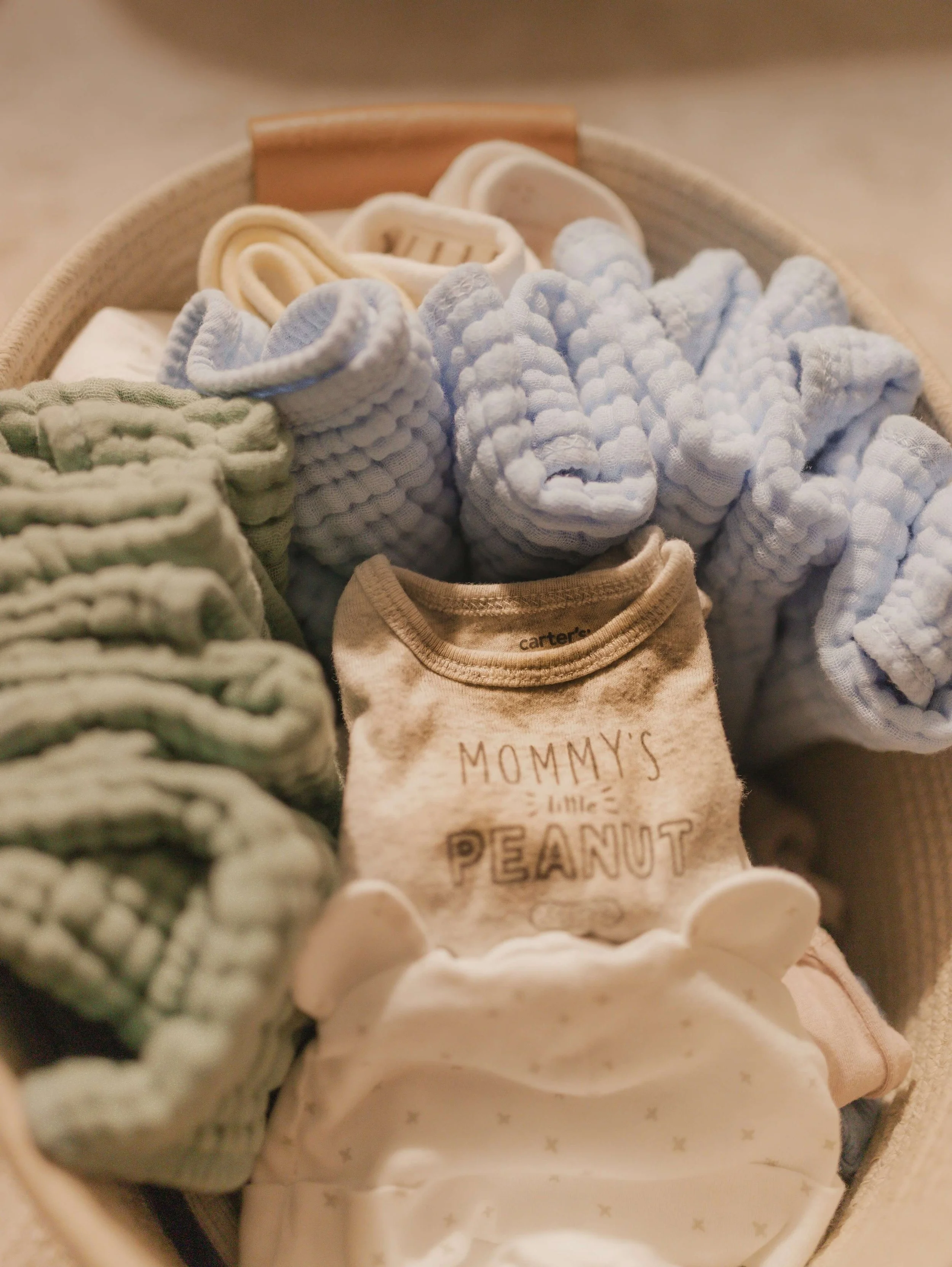 Folded infant clothes and cloth diapers in a woven basket.