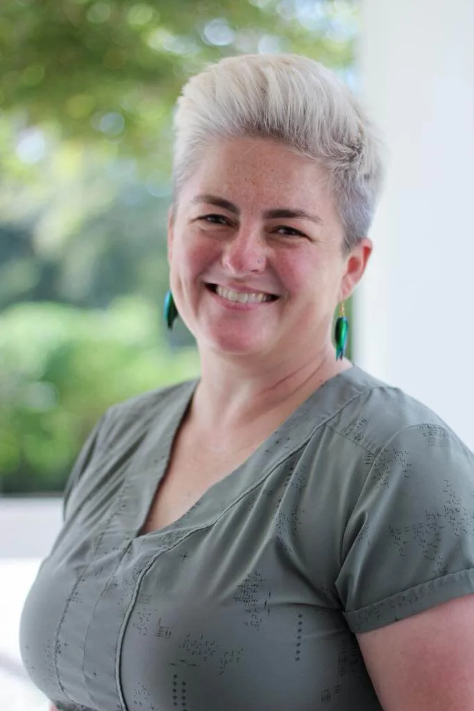 Postpartum doula Wendy Black smiles and wears a sage shirt with greenery in the background.