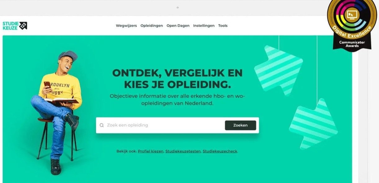 Een jongeren man zit op een stoel, draagt een gele hoodie en een grijze pet, lacht terwijl hij op een smartphone kijkt. Op de website van Studiekeuze123 met een groene achtergrond en tekst 'Ontdek, vergelijk en kies je opleiding'.