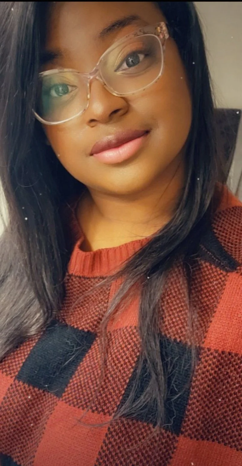 A woman with long black hair wearing glasses with clear frames and a red and black plaid sweater.