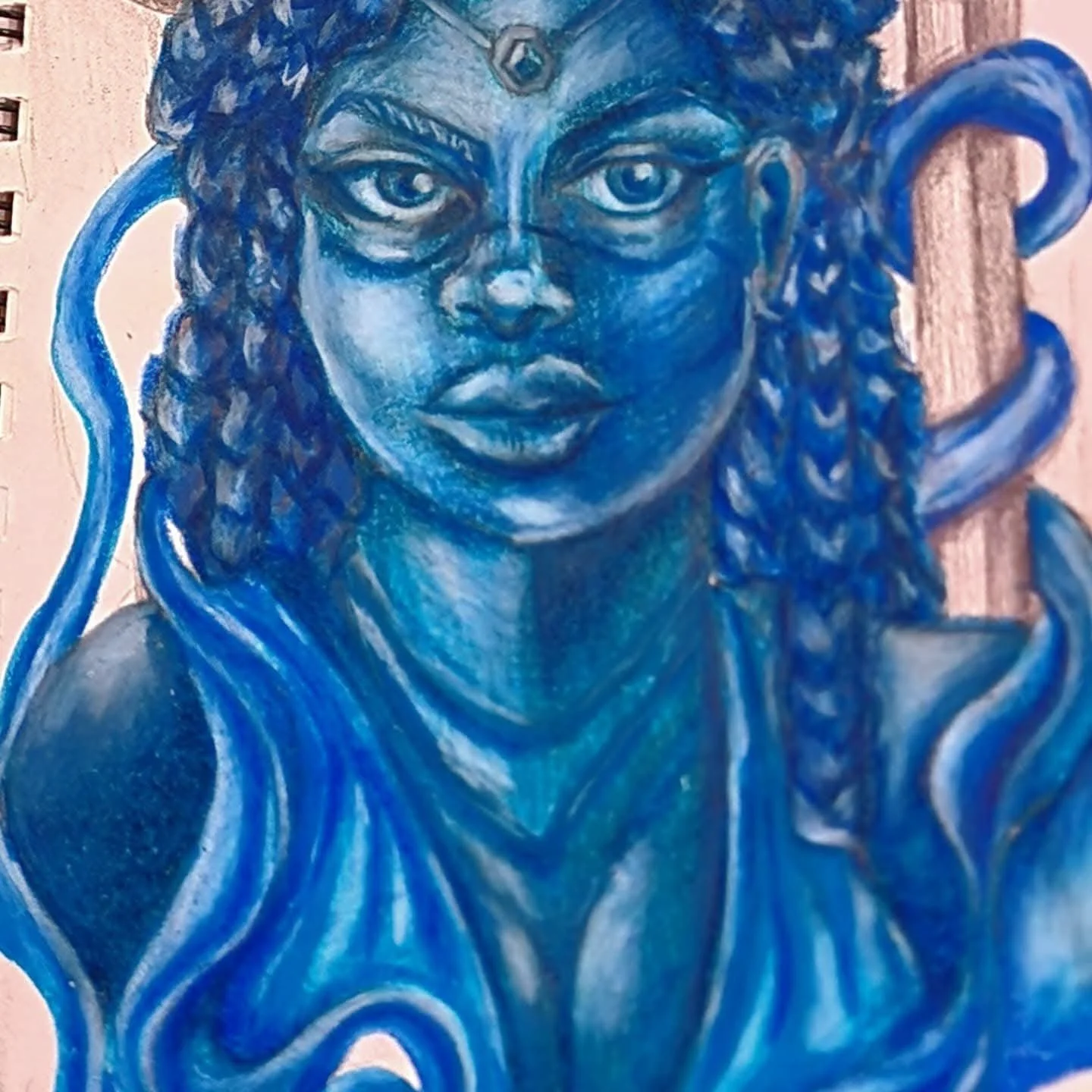 A mural of a woman painted in shades of blue, with large expressive eyes, curly hair, and a jewel on her forehead, set against a brick wall background.
