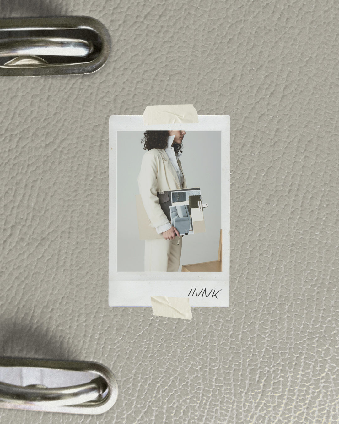 Polaroid photo taped to a beige textured surface, showing a woman in cream-colored clothing holding a collage of interior design images.
