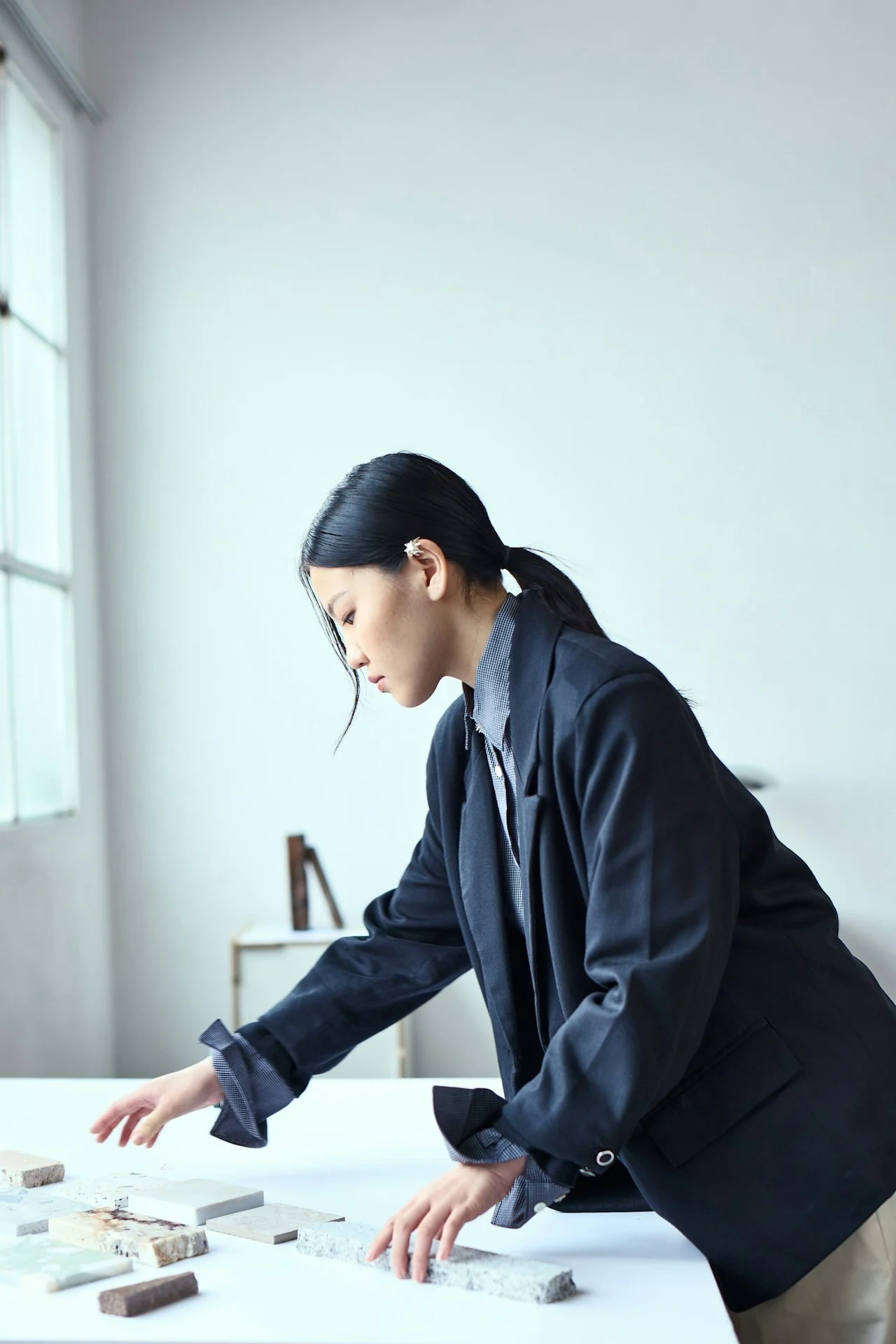 A woman working at a white table with scattered paper clips, thumbtacks, and papers, with a background featuring multiple overlapping black-and-white photographs.