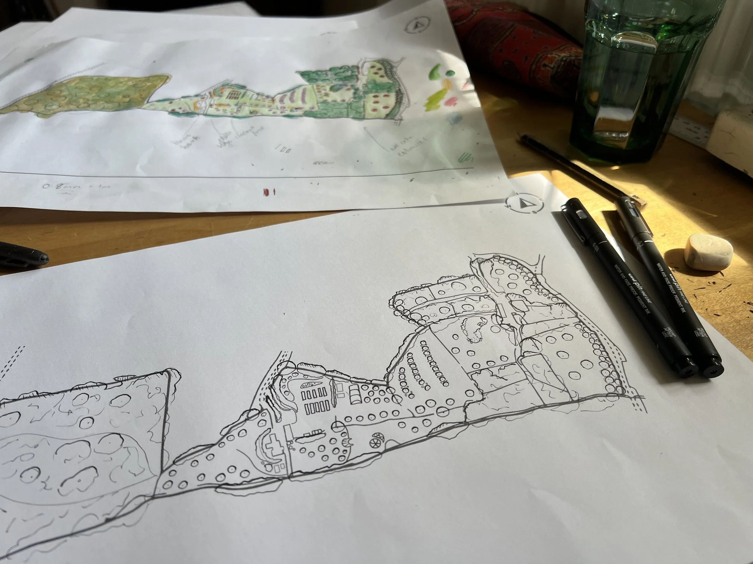 Architectural drawings on sheets of paper with markers, a glass of water, and a pencil on a wooden table.