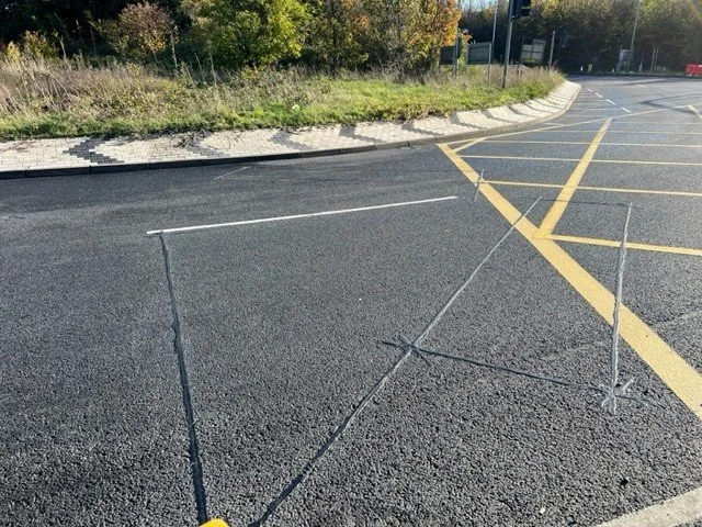 A parking lot with a makeshift chessboard made from thin, black string arranged in a 3x3 grid, with yellow parking lines and some greenery in the background.