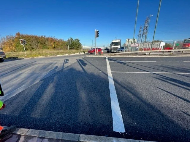 View of a busy intersection with traffic lights and multiple vehicles, including trucks and cars, on a sunny day.