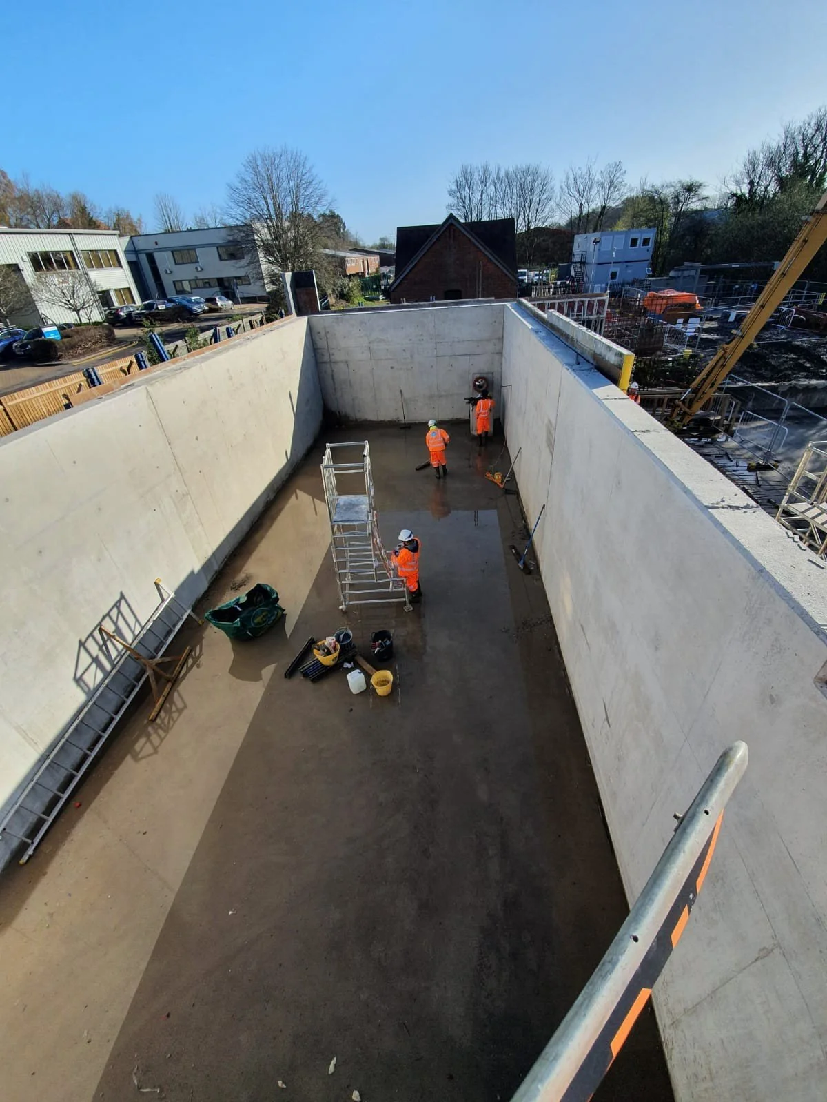 Construction site with workers installing a concrete floor, surrounded by tall concrete walls and building equipment.
