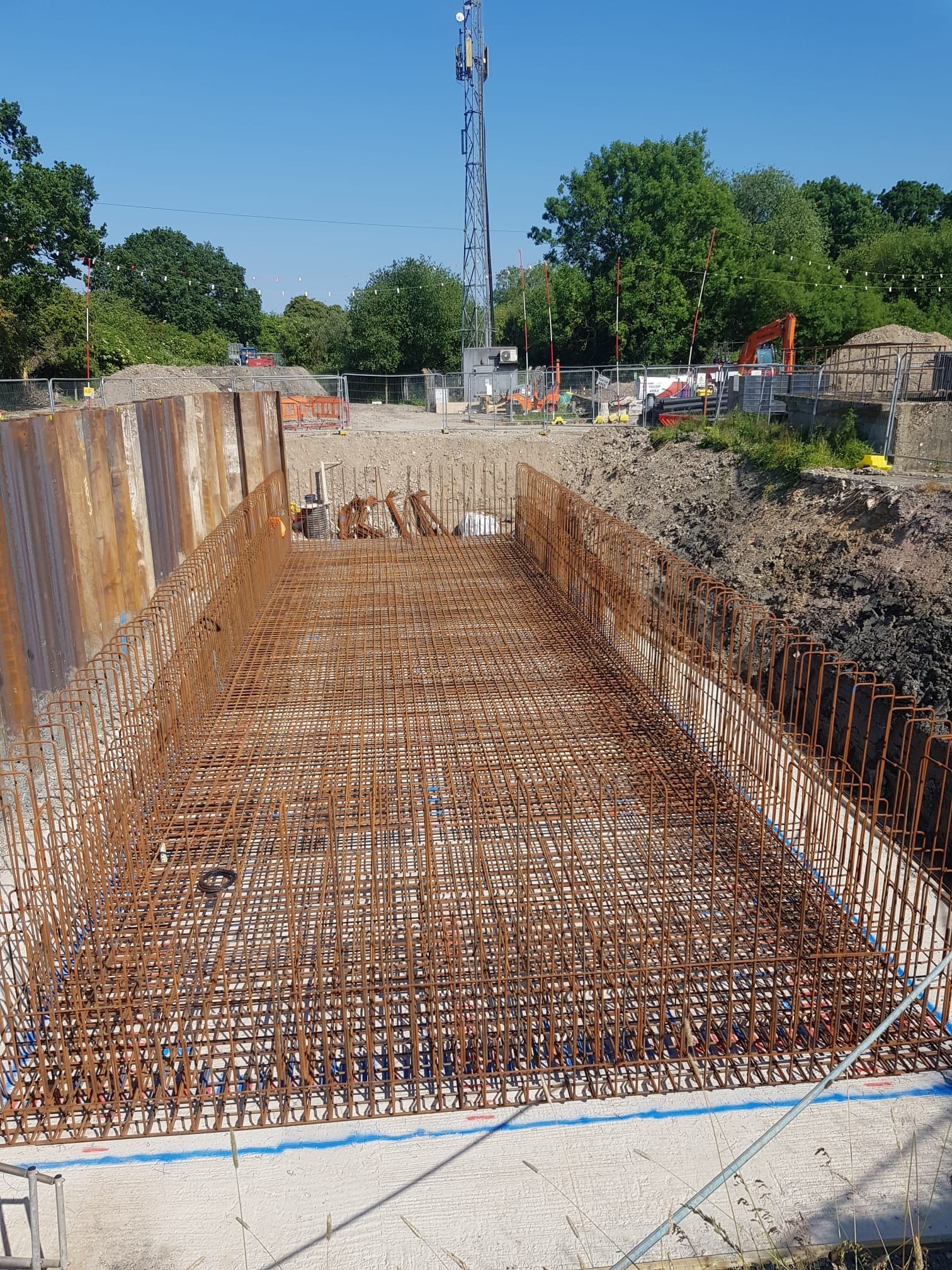 Construction site showing rebar reinforcement in foundation, with scaffolding and construction equipment in the background.