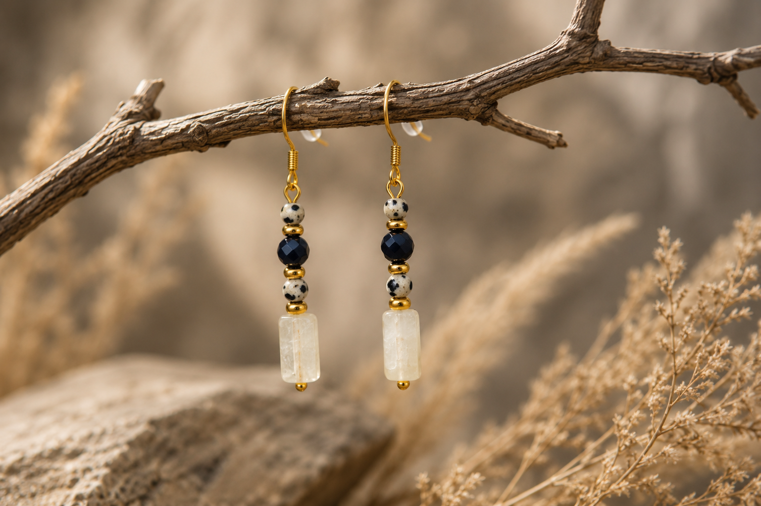 Gold and black beaded dangle earrings hanging from a tree branch with a blurred natural background.