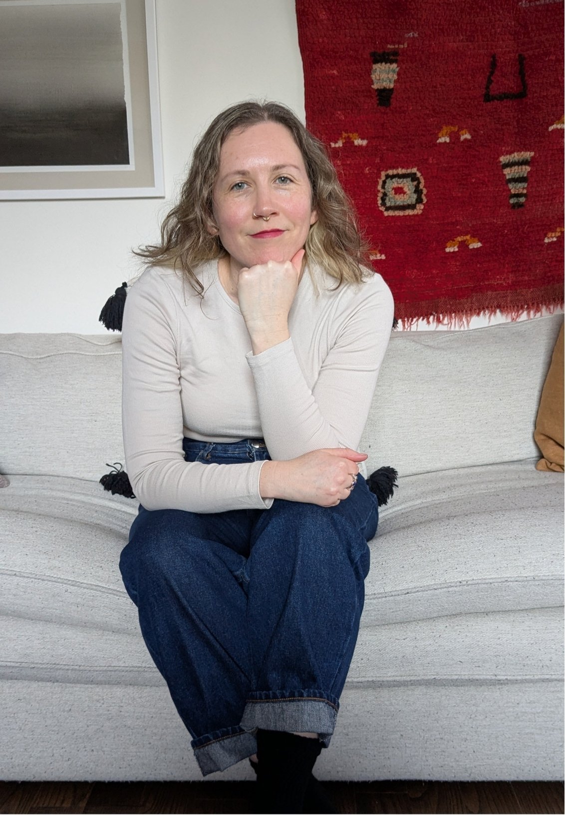 Amelia Sloan, therapist in Guelph, sits on a gray coach smiling at the camera.