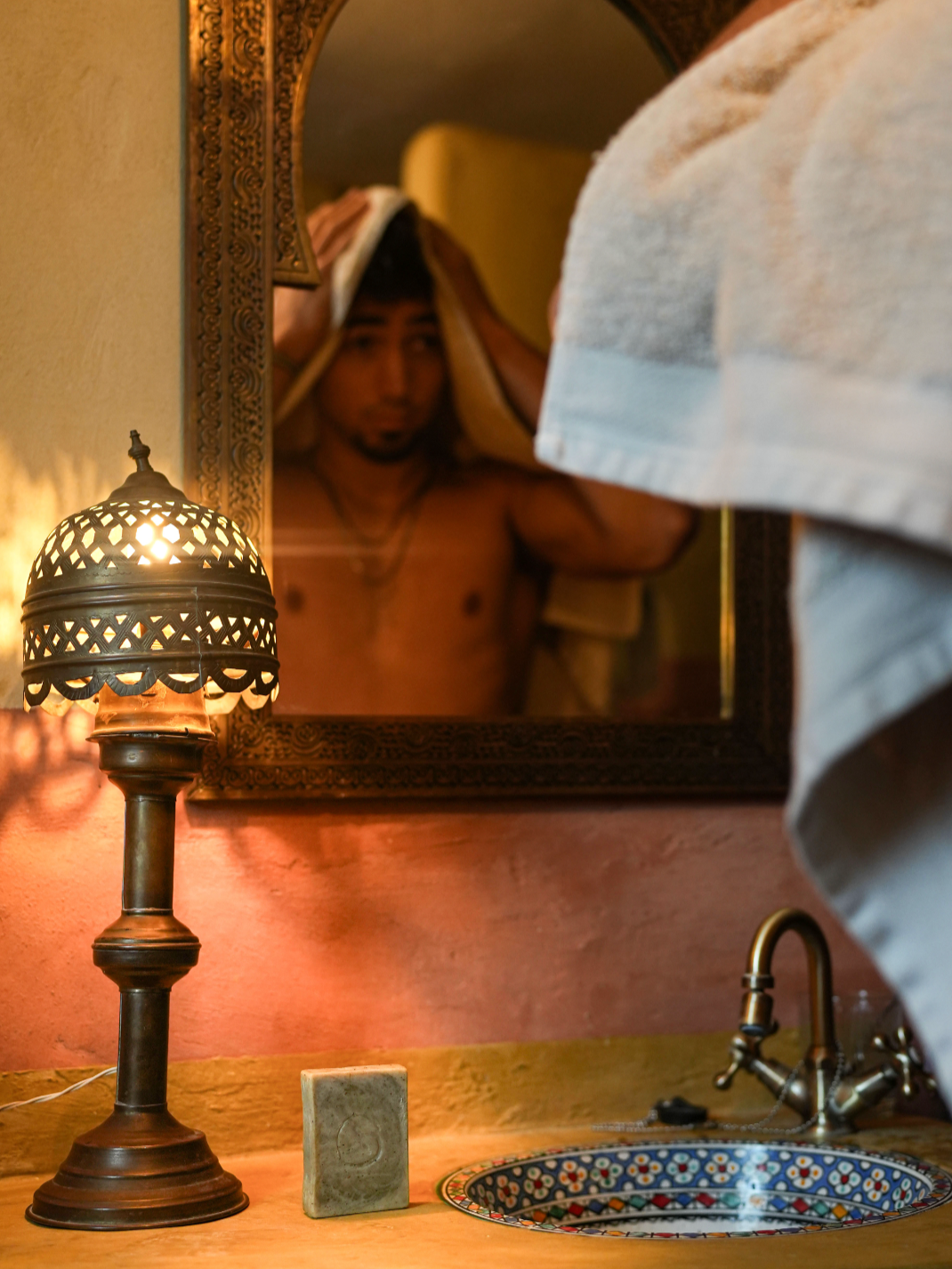 Hombre mirándose en un espejo, sujetándose la cabeza, un jabon para el cabello de Ajedrea Cosmetica Ecologica esta en el fregadero.