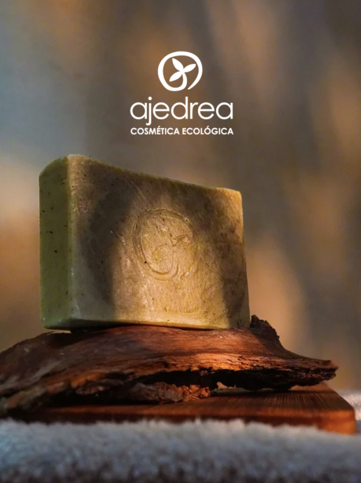 Jabón ecológico de la marca Ajedrea con logo y fondo difuso, sobre una base de madera y superficie texturizada.