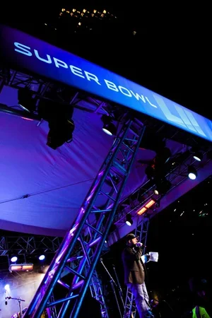 Stage with a Large screen displaying 'SUPER BOWL' and superimposed Roman numeral 'L' at an indoor event.
