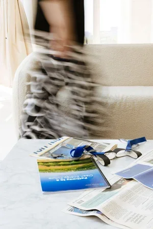 Blurred image of a person in motion, with scattered magazines, a book, and lanyards on a table in a living room setting.