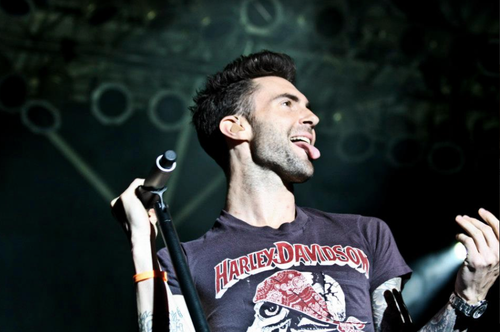 Adam Levine of Maroon 5 sings on stage with microphone, wearing a Harley Davidson t-shirt, singing with a passionate expression.
