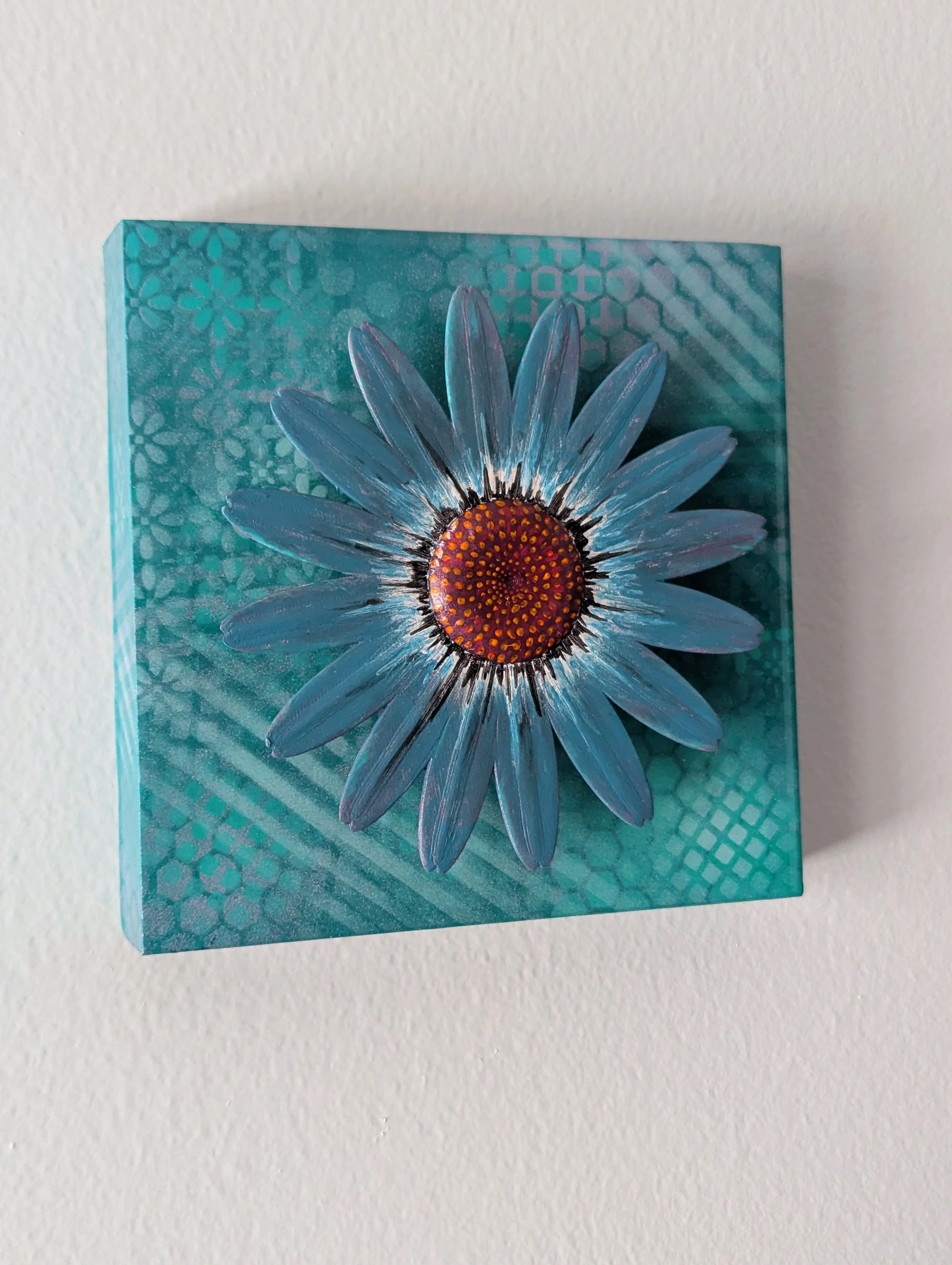 Decorative teal painting featuring an elevated blue flower on a patterned teal background.
