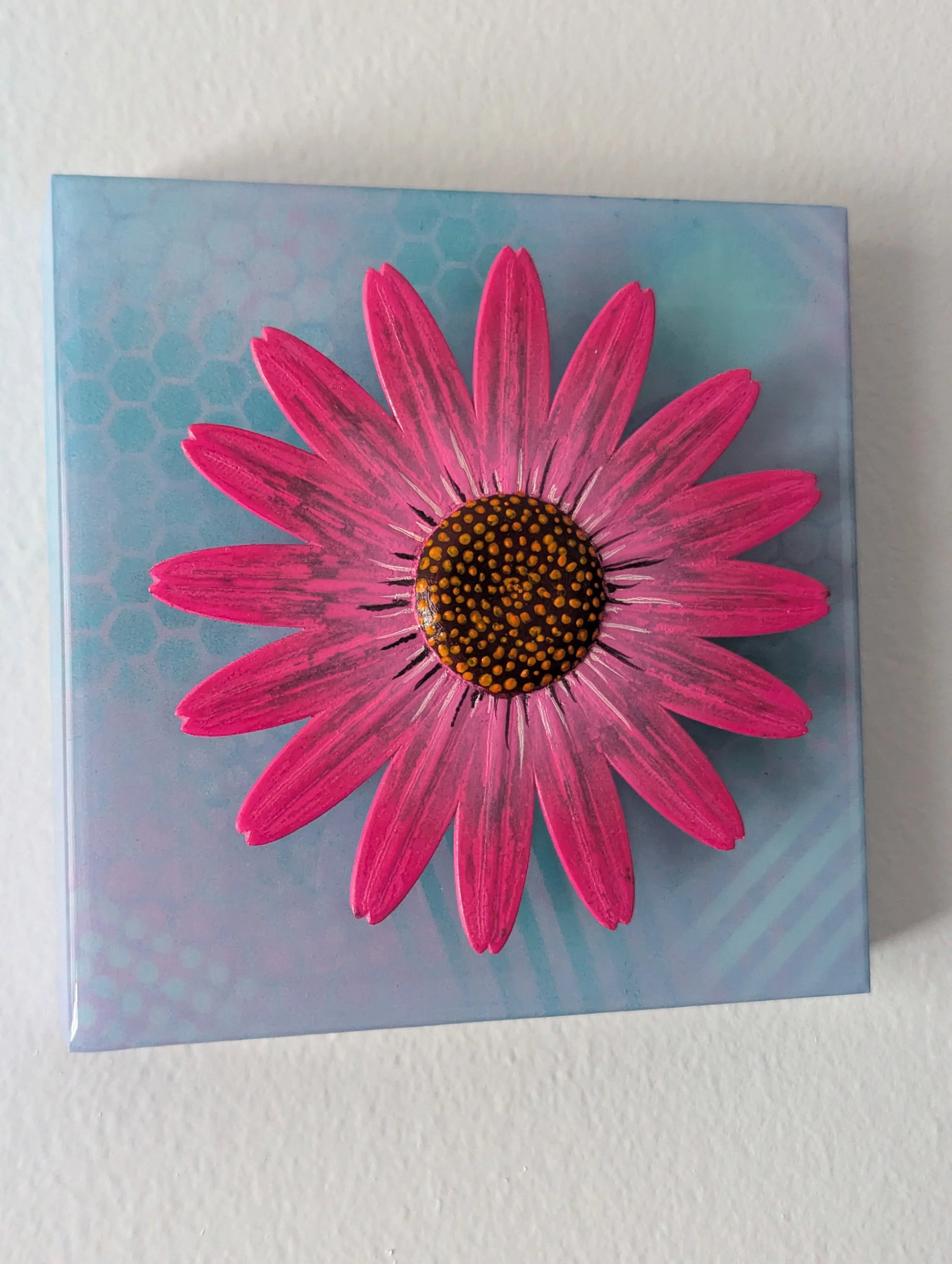 Decorative blue painting with a elevated pink daisy flower on it.