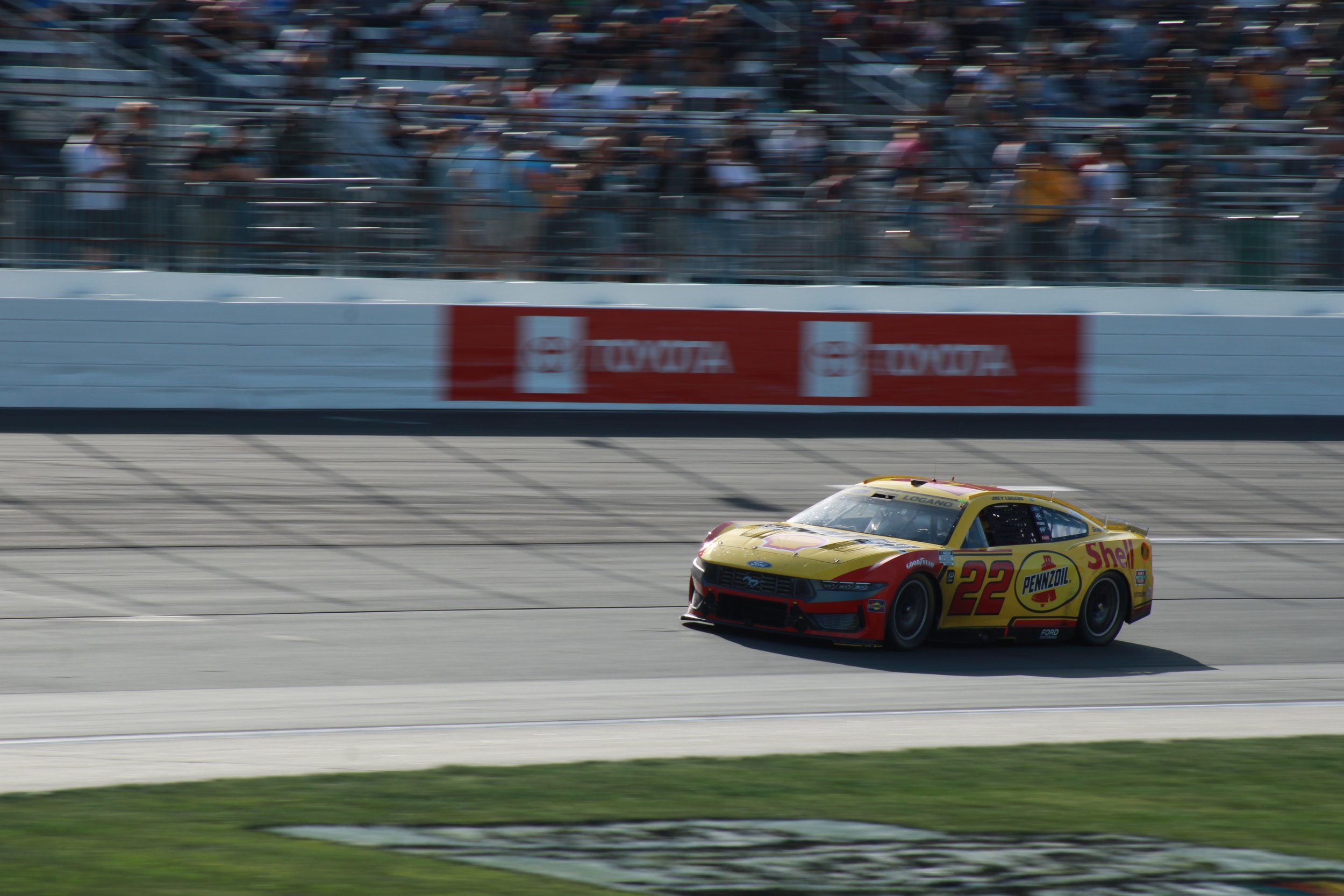 A yellow and red race car number 22 speeds along a racetrack with blurred spectators in the background.