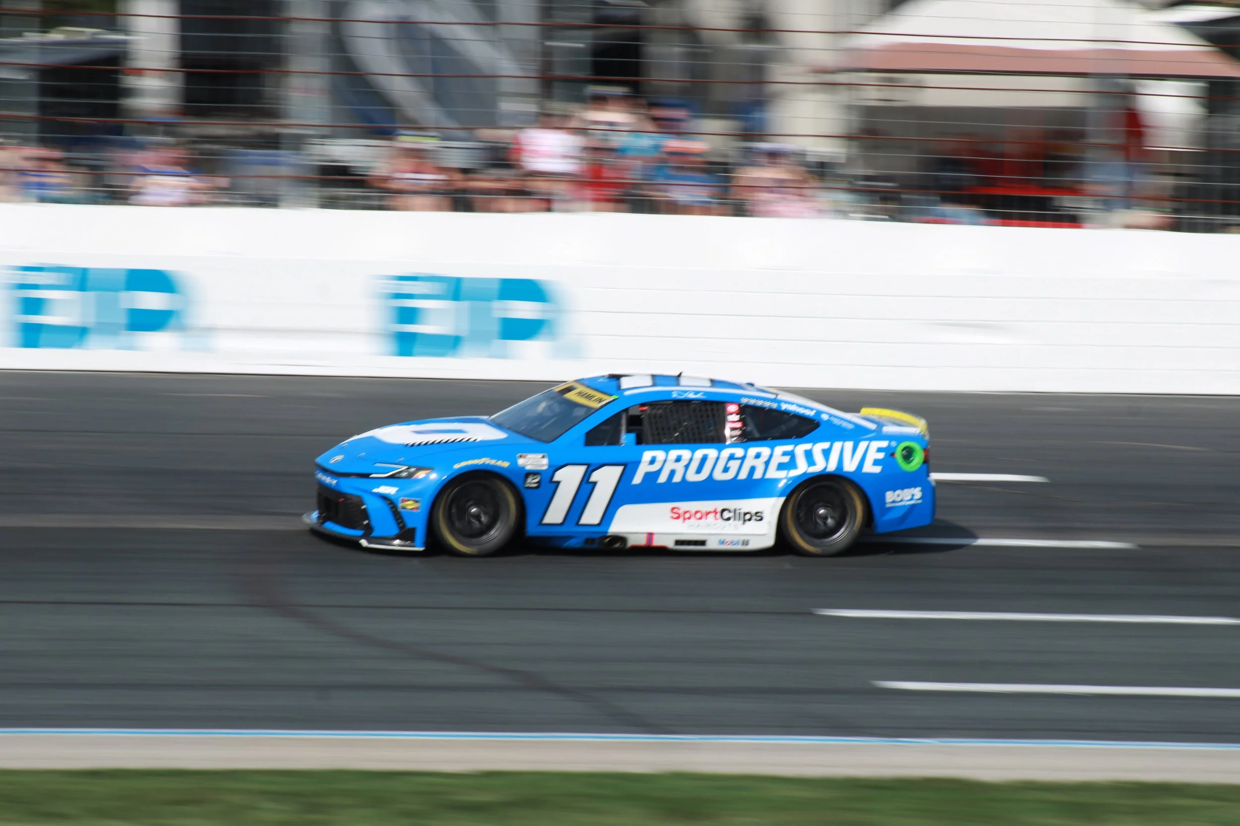 A blue race car with the number 11 and featured sponsors, including Progressive, speeding along a race track during a race event.