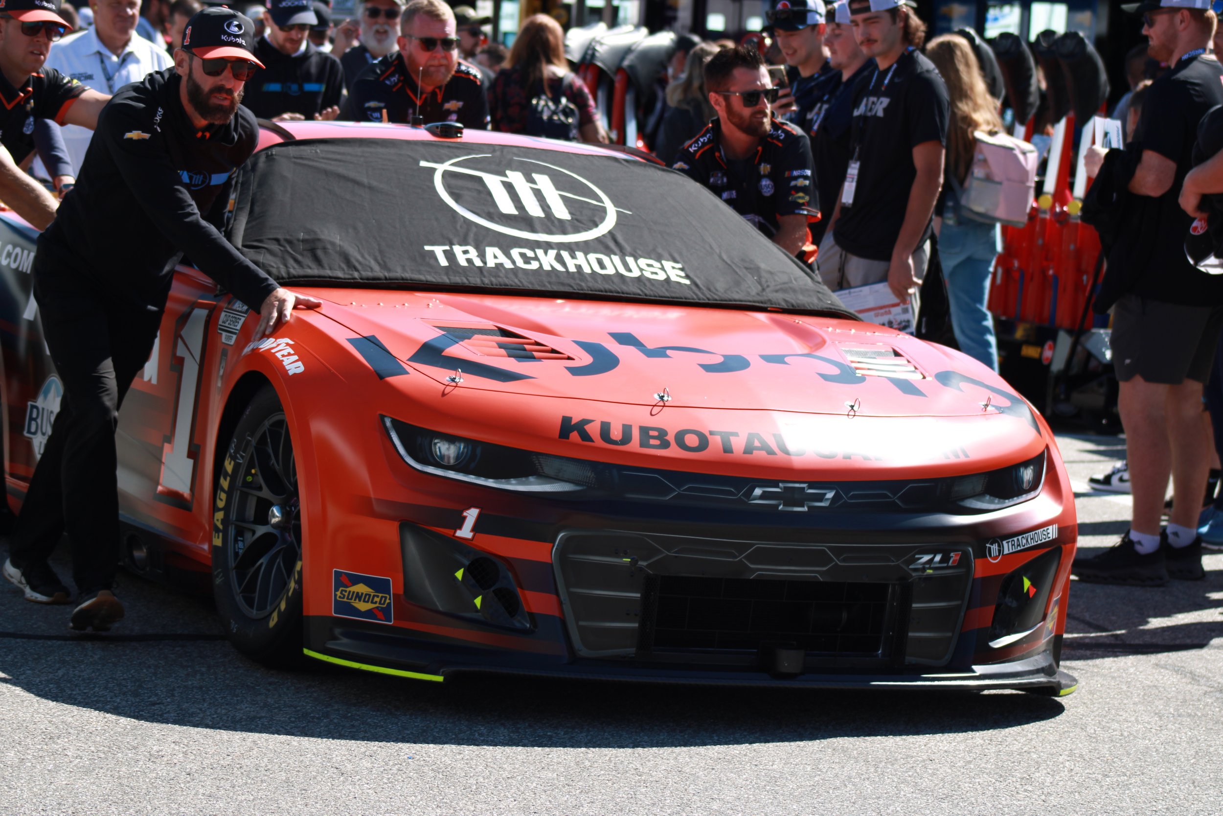 A red race car with the number 1 and various sponsor logos, including Chevrolet and Sunoco, surrounded by a crowd of people at a racing event.