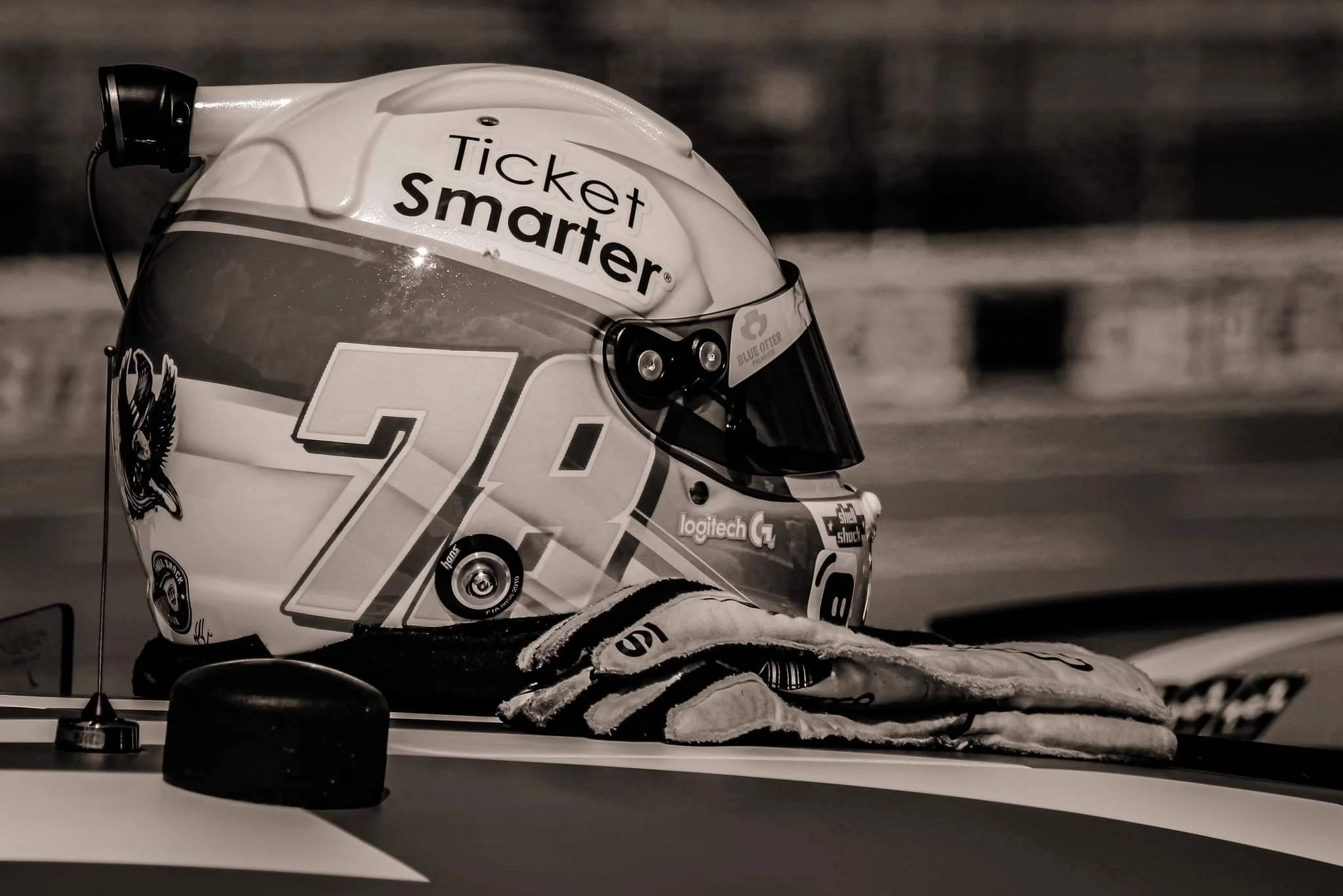 A racing helmet with the number 20 and stickers on it, resting on a race car with a pair of gloves nearby.