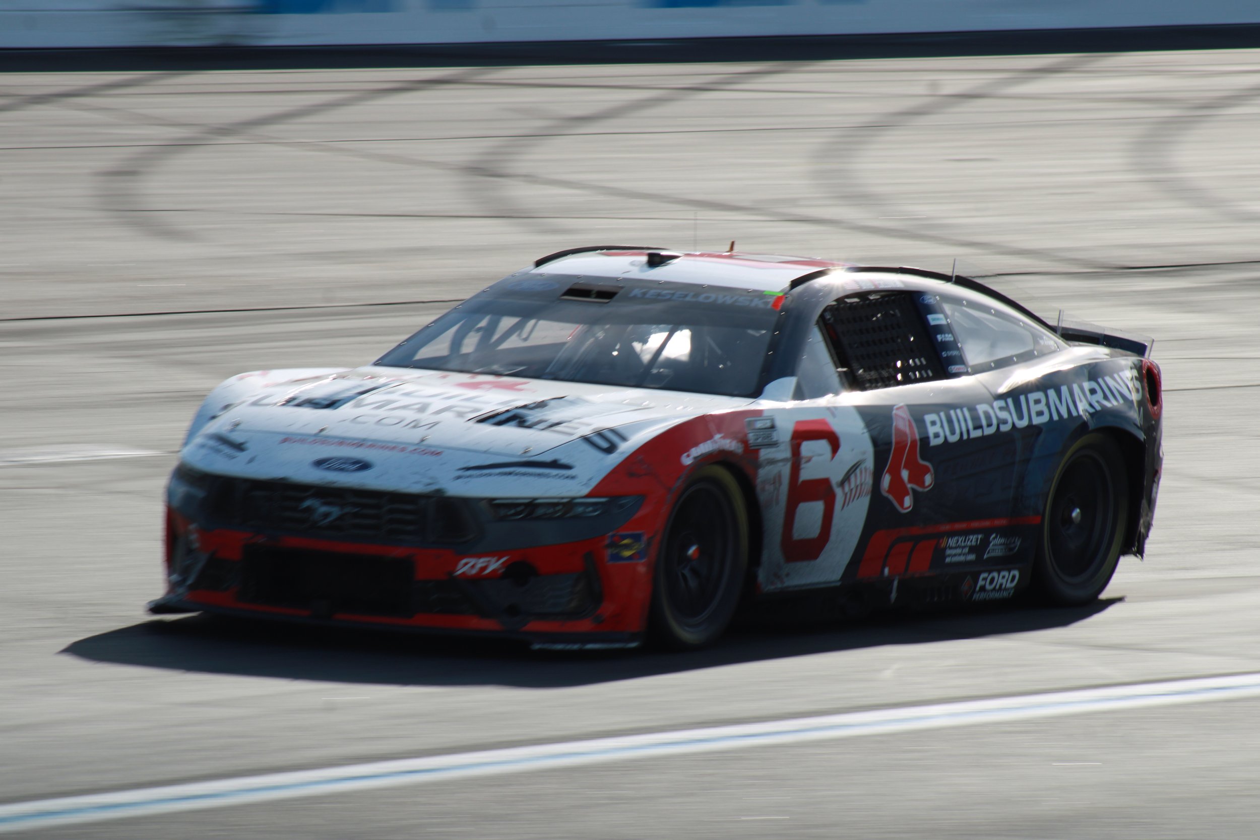 A racing car on a racetrack with a white, red, and black paint scheme, featuring the number 6 and sponsor logos.