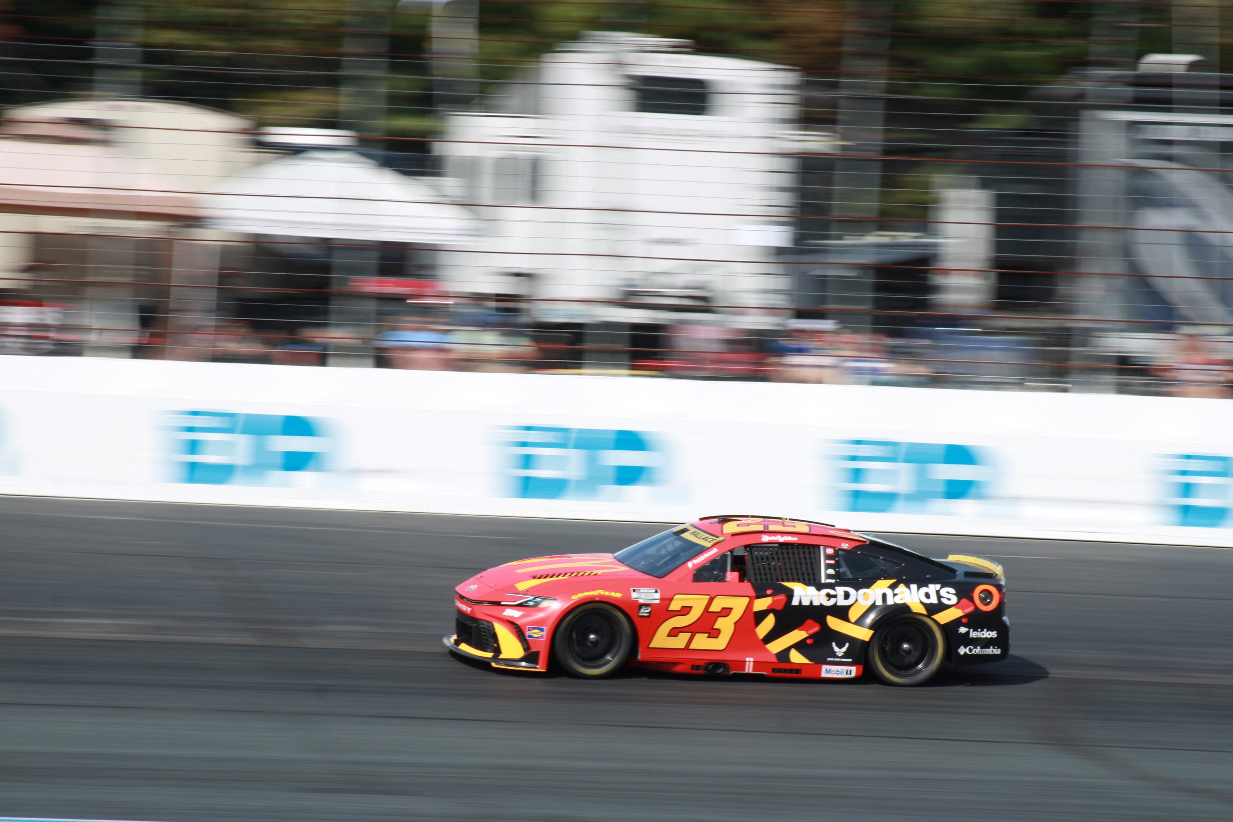 A red and black race car with the number 23, sponsored by McDonald's, racing on a track with a blurred background.