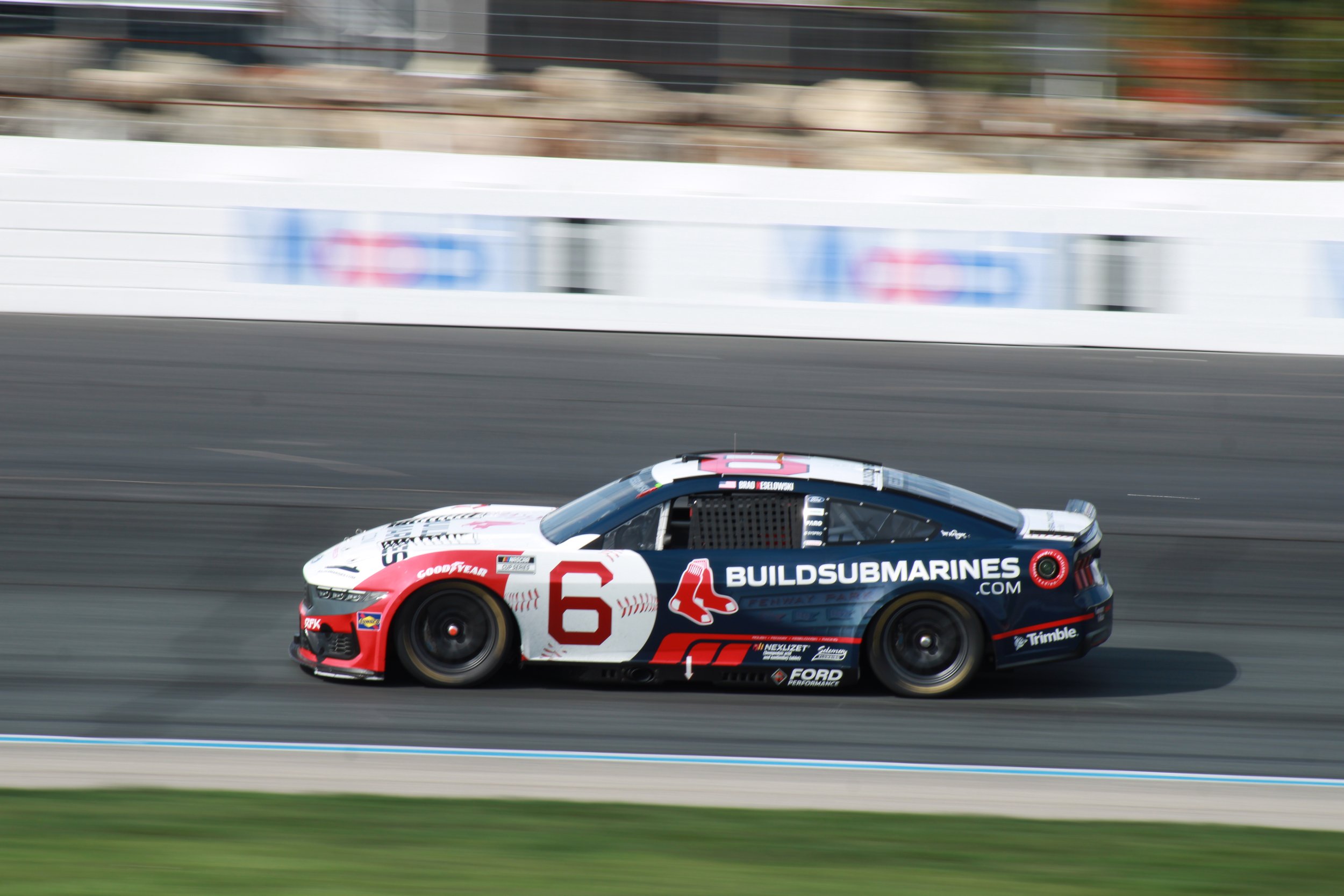 A race car with the number 6 on the side, sponsored by Build Submarines, racing on a track with a blurred background.