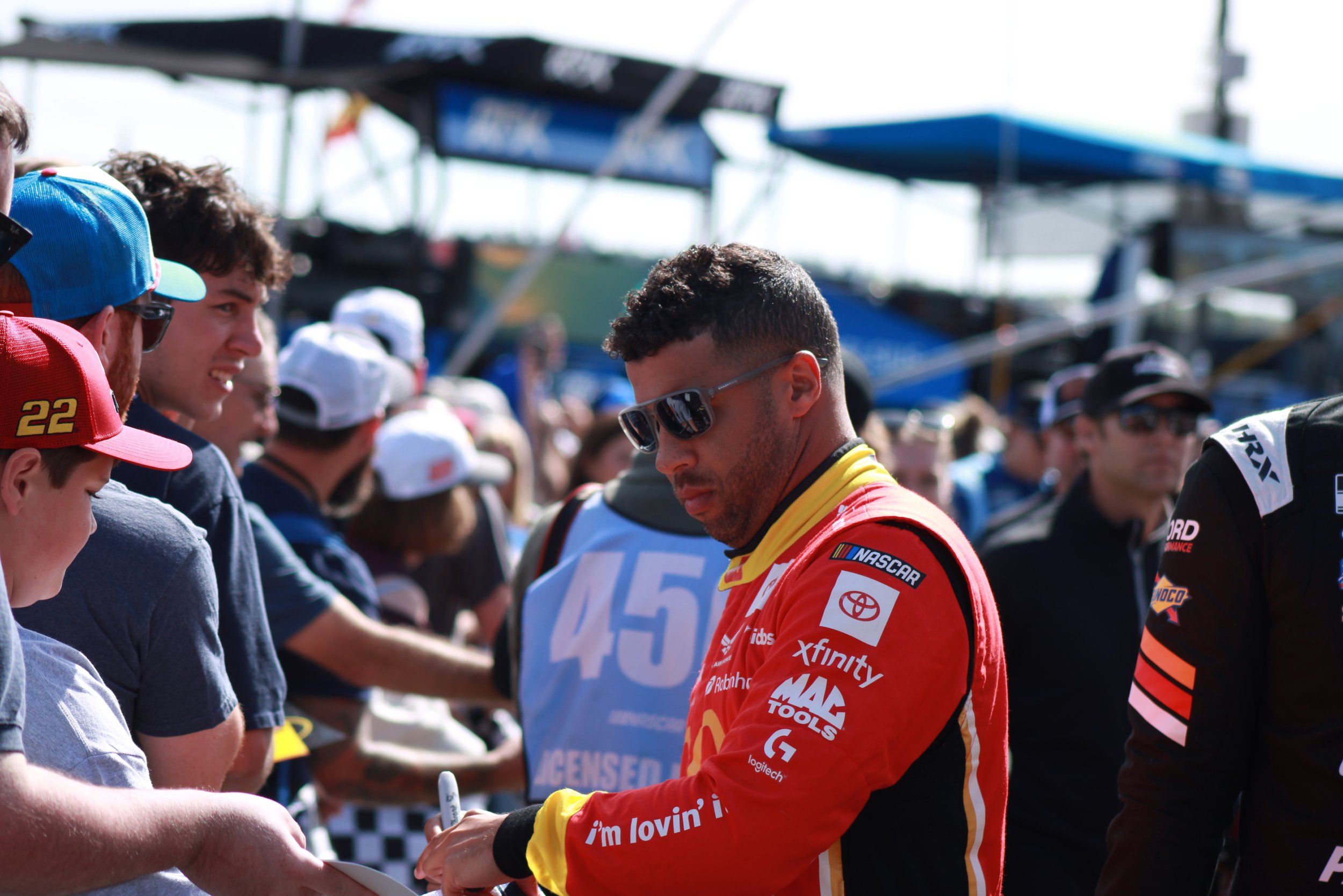 NASCAR driver signing autographs for fans at an outdoor event.