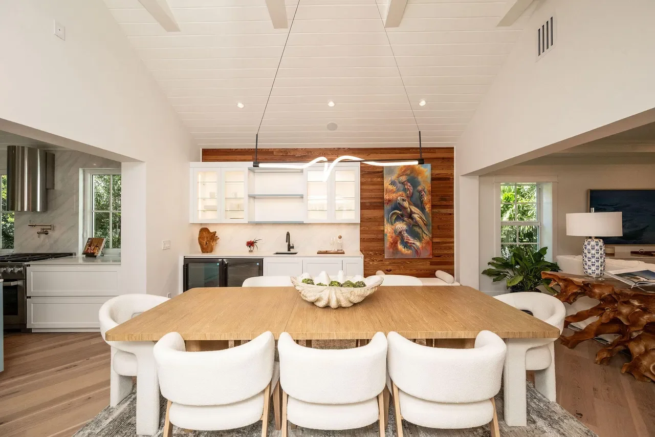 Key West coastal dining room featuring a solid wood dining table, sculptural pendant lighting, white cabinetry, Dade county pine accent wall, and airy Florida Keys design.