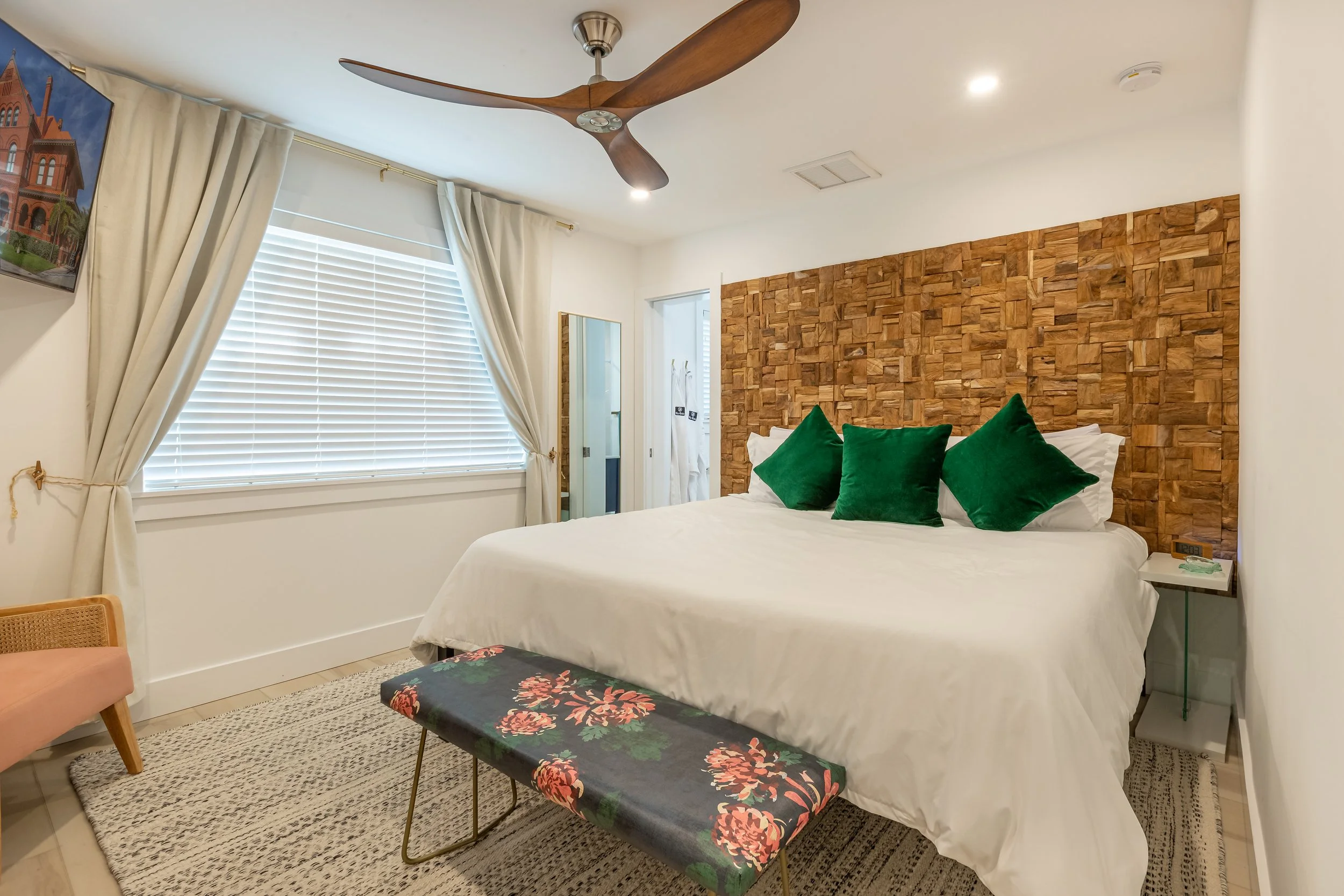 Key West bedroom with textured wood accent wall, white bedding, green accent pillows, ceiling fan, and relaxed Florida coastal design.
