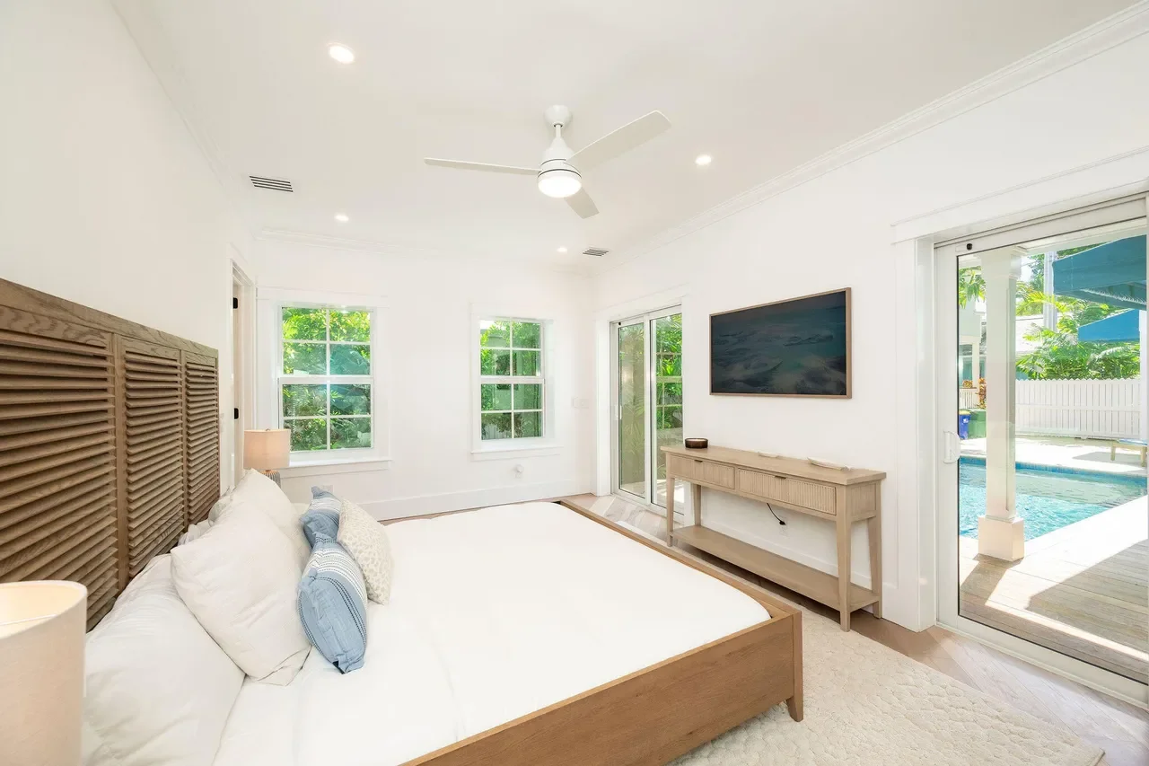 Primary Key West bedroom with sliding glass doors to a private pool, white walls, light wood floors, coastal furnishings, and seamless indoor-outdoor living.