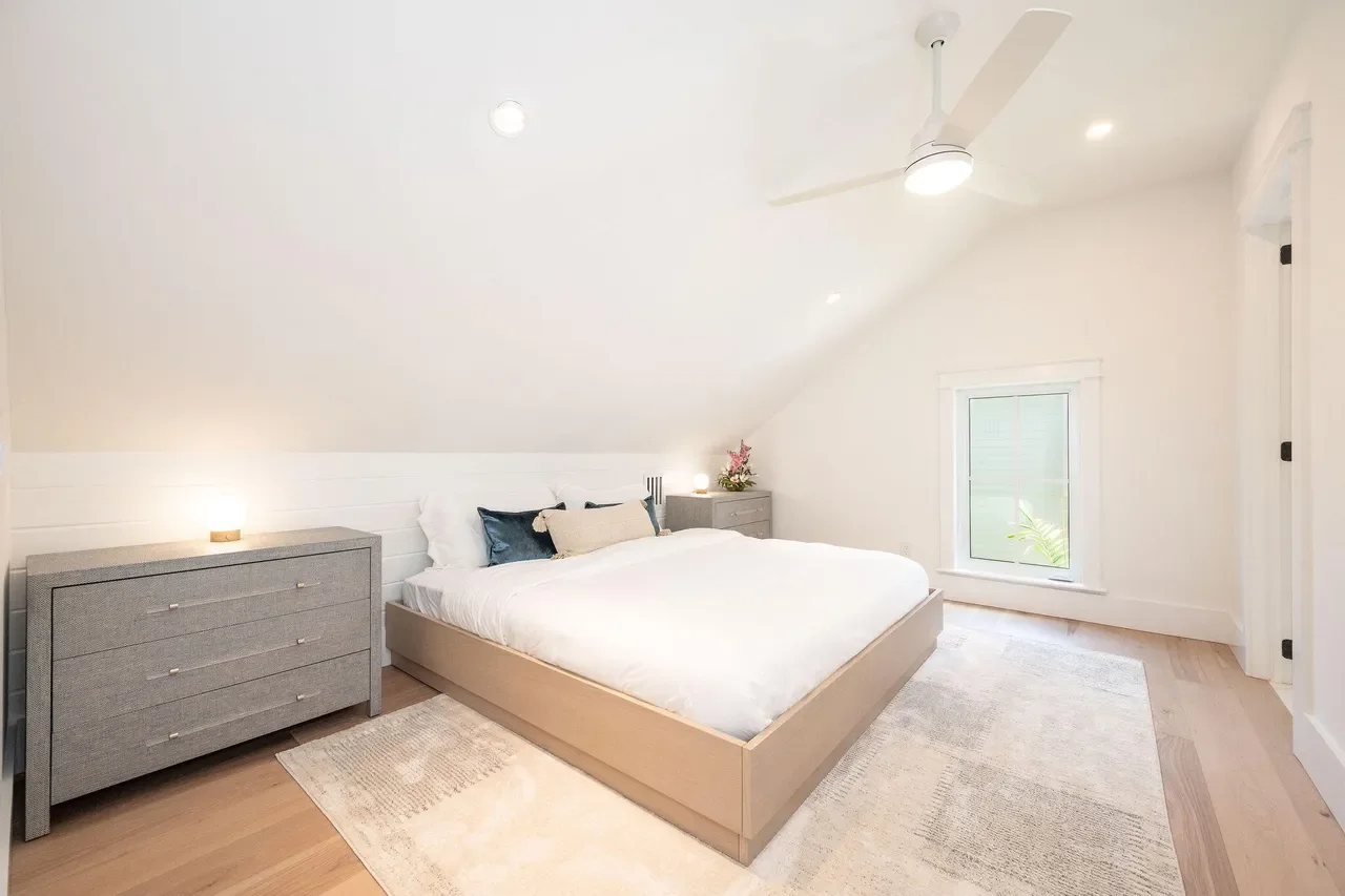 Bright Key West guest bedroom with vaulted ceiling, white walls, minimalist coastal furnishings, light wood floors, and ceiling fan for relaxed island comfort.