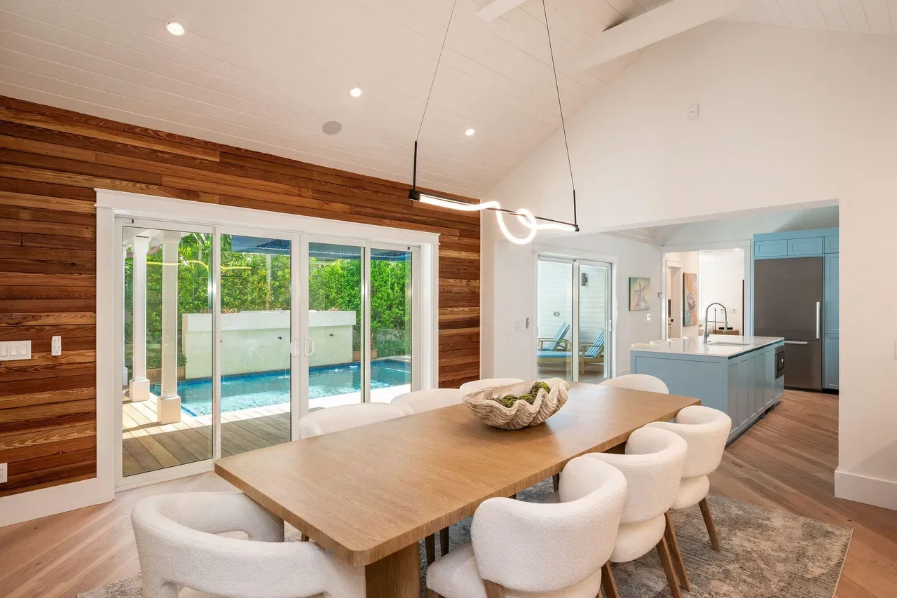 Open-concept Key West dining space with vaulted white ceiling, natural wood accent walls, indoor-outdoor living design, and a seamless connection to a Florida tropical pool and patio.