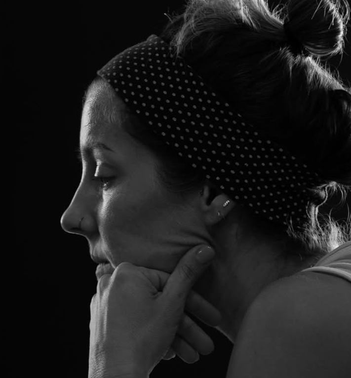 Black and white photo of a woman in profile, resting her chin on her hand, with her eyes closed, wearing a polka dot headband.