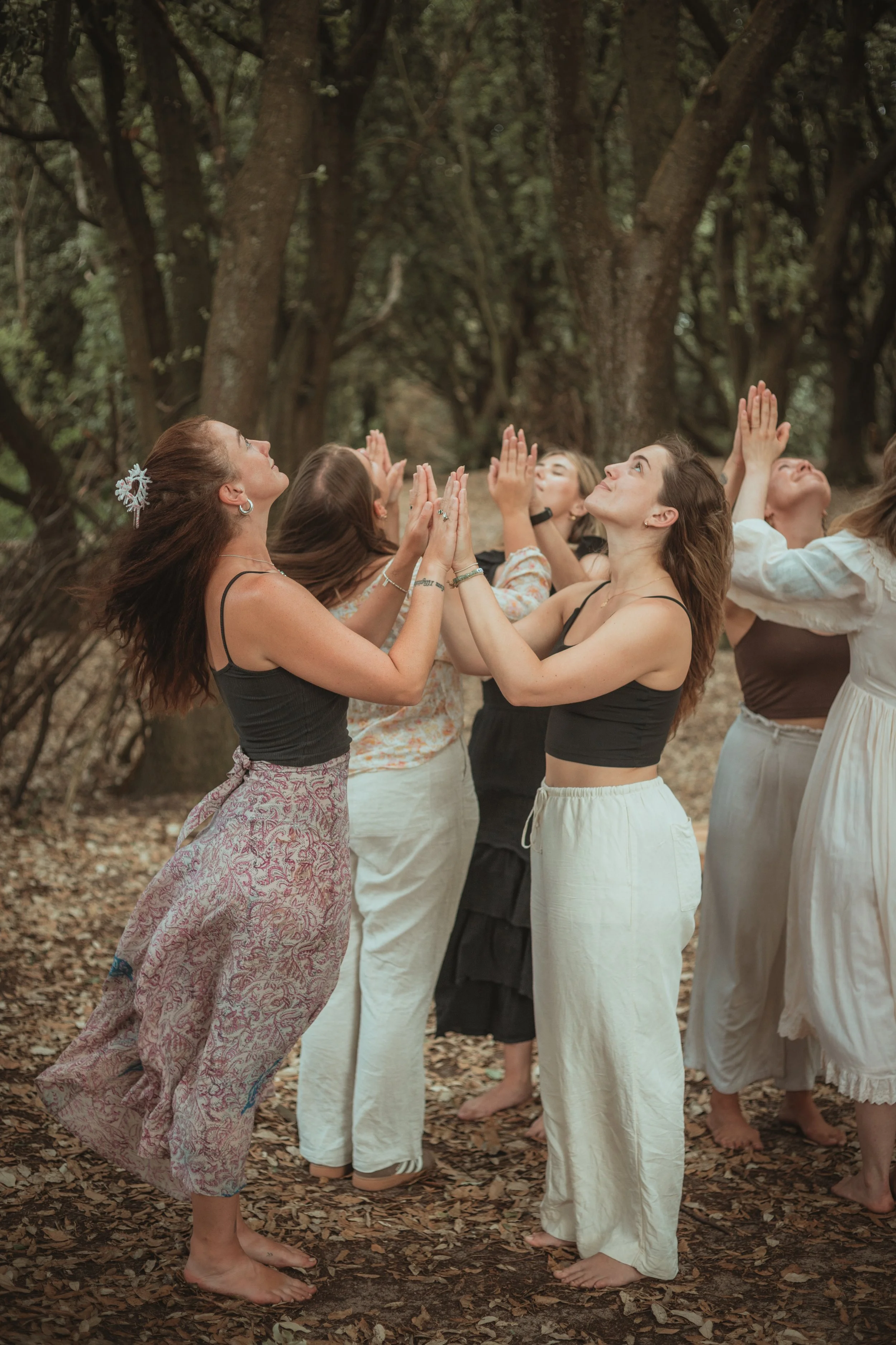 Group of women with arms raised in a forest setting, appearing to perform a ritual or dance