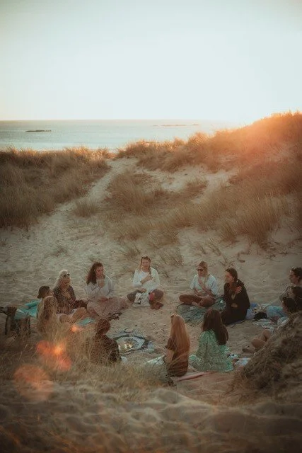 Group of people sitting in a circle on the beach during sunset.