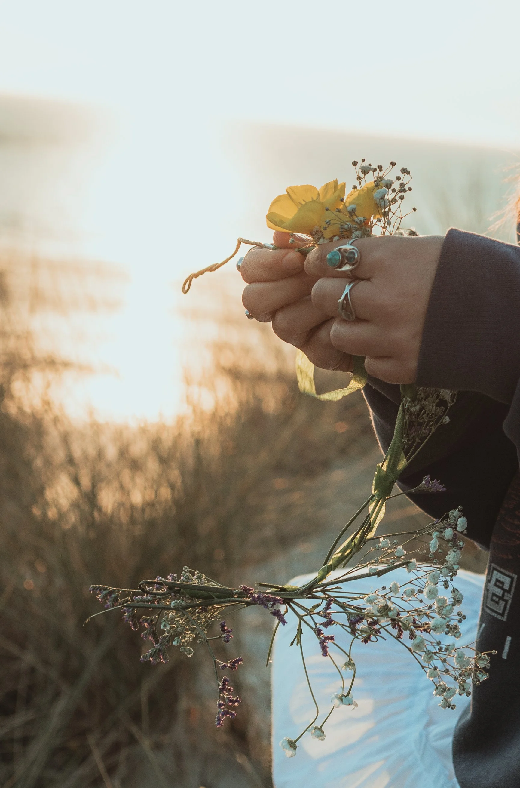 Person holding a small bouquet of wildflowers with a sunset in the background.