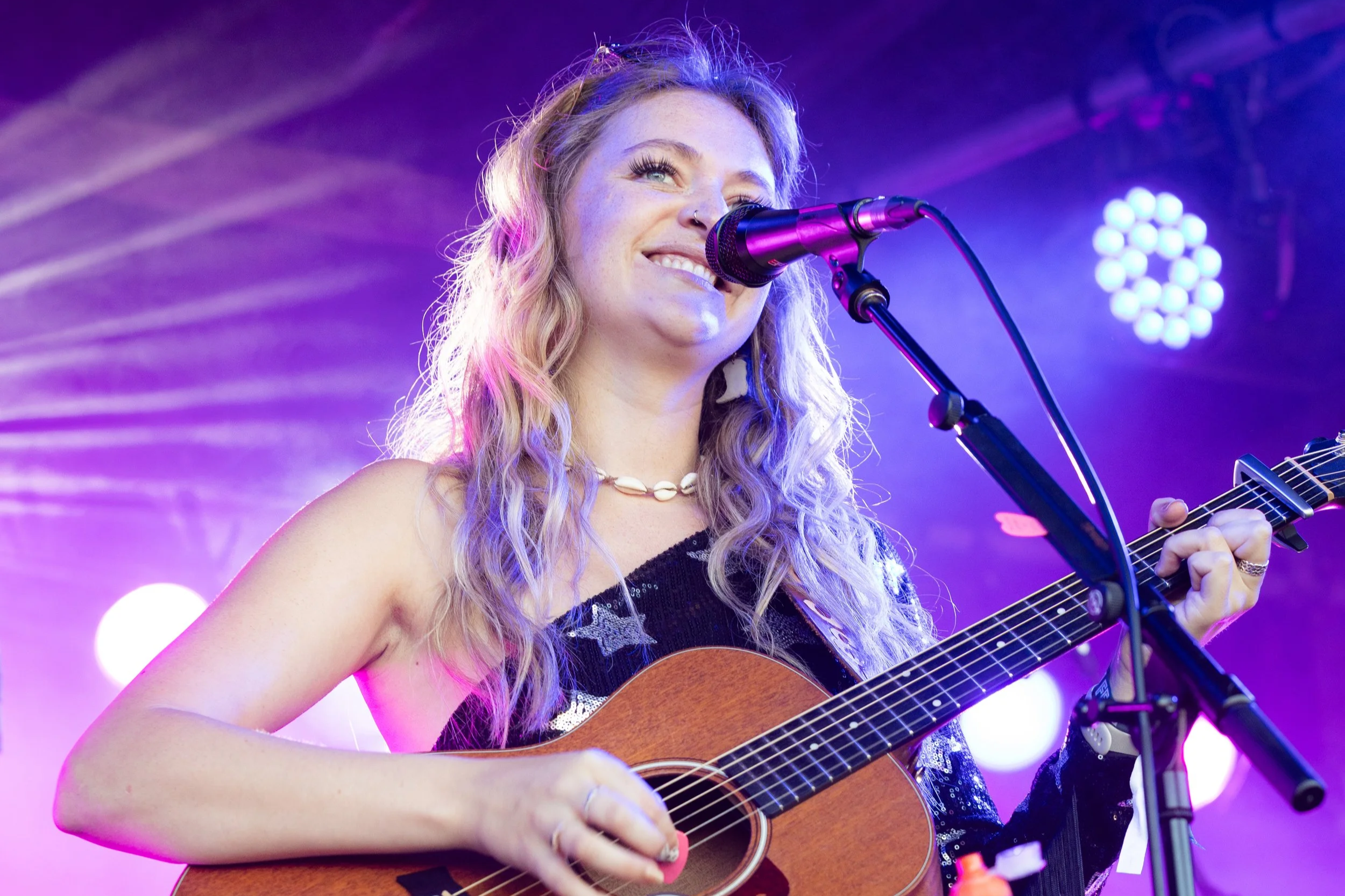 Louise Parker performing live with an acoustic guitar at a country pop gig, singing on stage at a UK live music event.