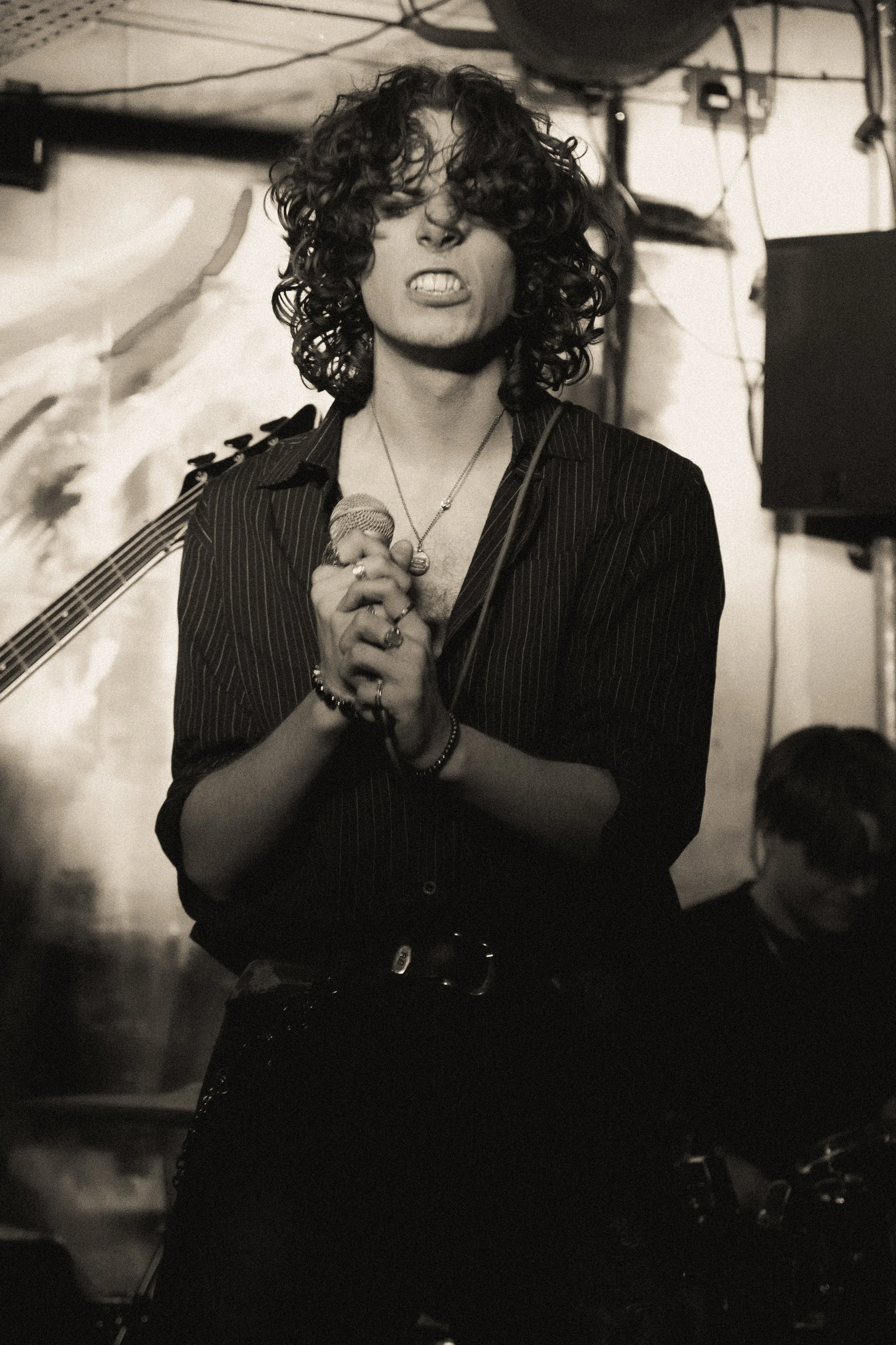 A woman with curly hair singing into a microphone on stage in a dimly lit setting.